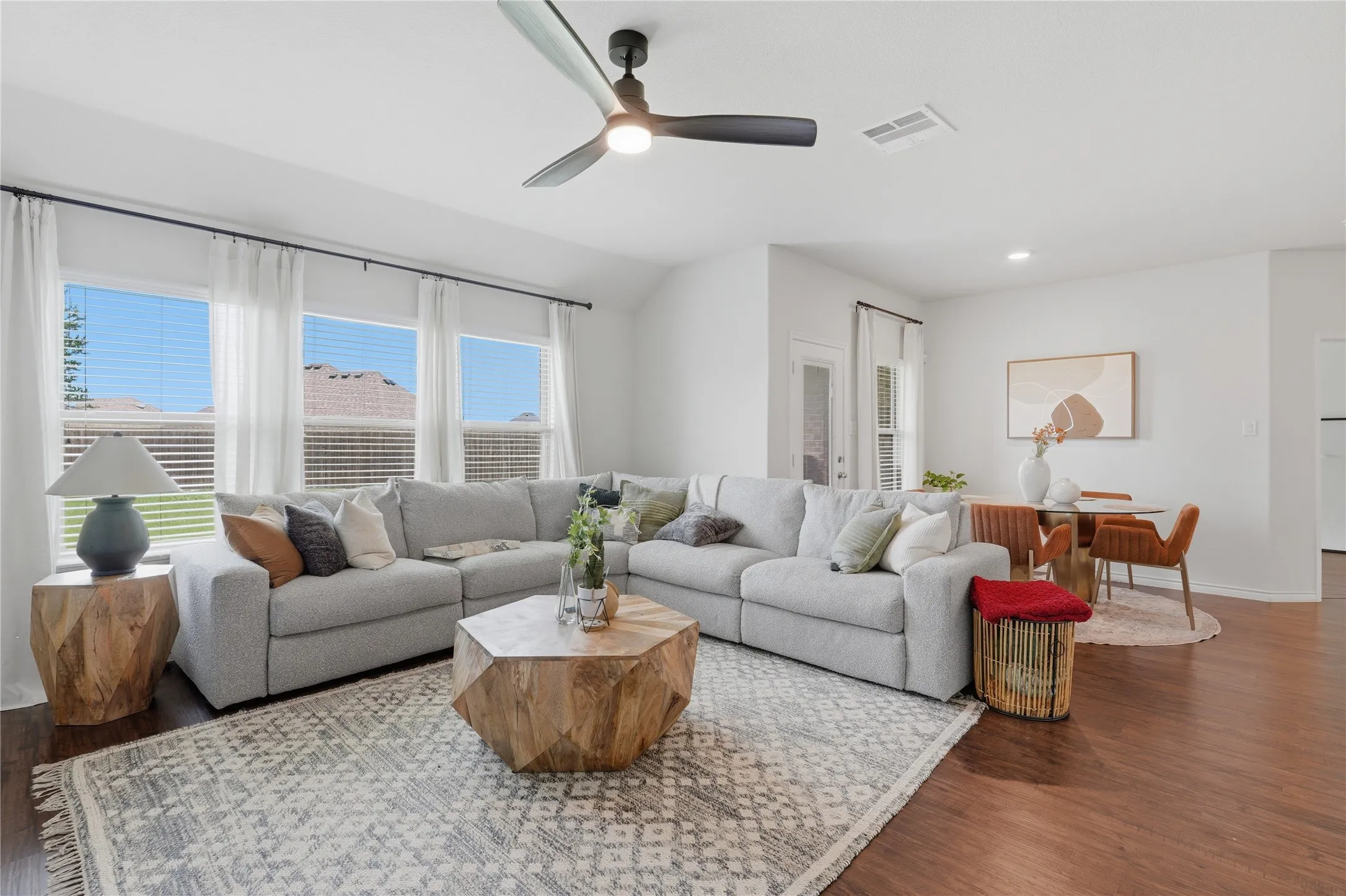 Open-concept living space featuring wood-finish flooring, multiple windows with blinds, and a ceiling fan