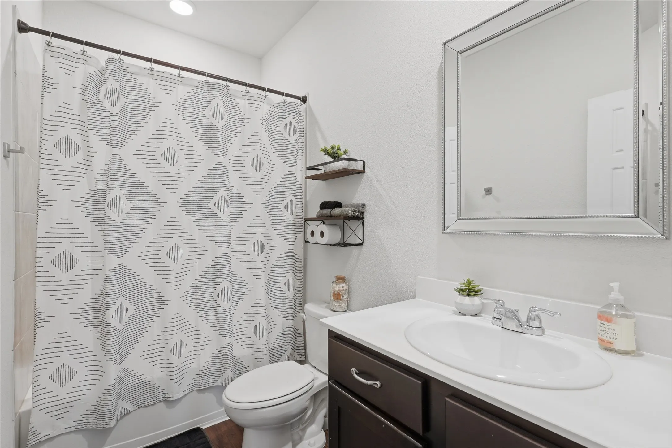Bathroom featuring a shower/tub combination with white tile surround, a dark wood-finish vanity with a white countertop and integrated sink, and a framed mirror
