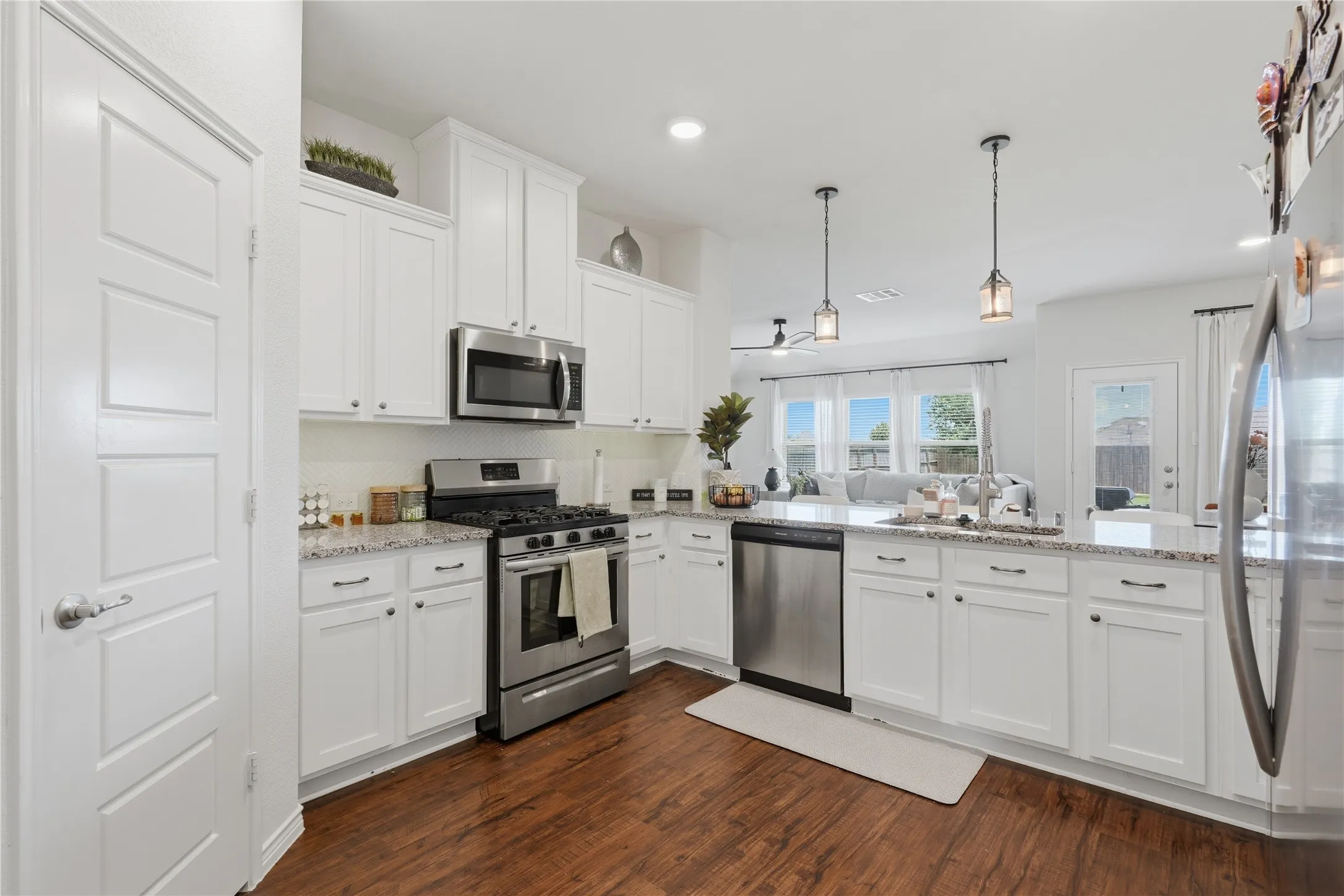 Contemporary kitchen featuring white cabinetry, stainless steel appliances, granite-style countertops, wood-finish flooring, and pendant lighting