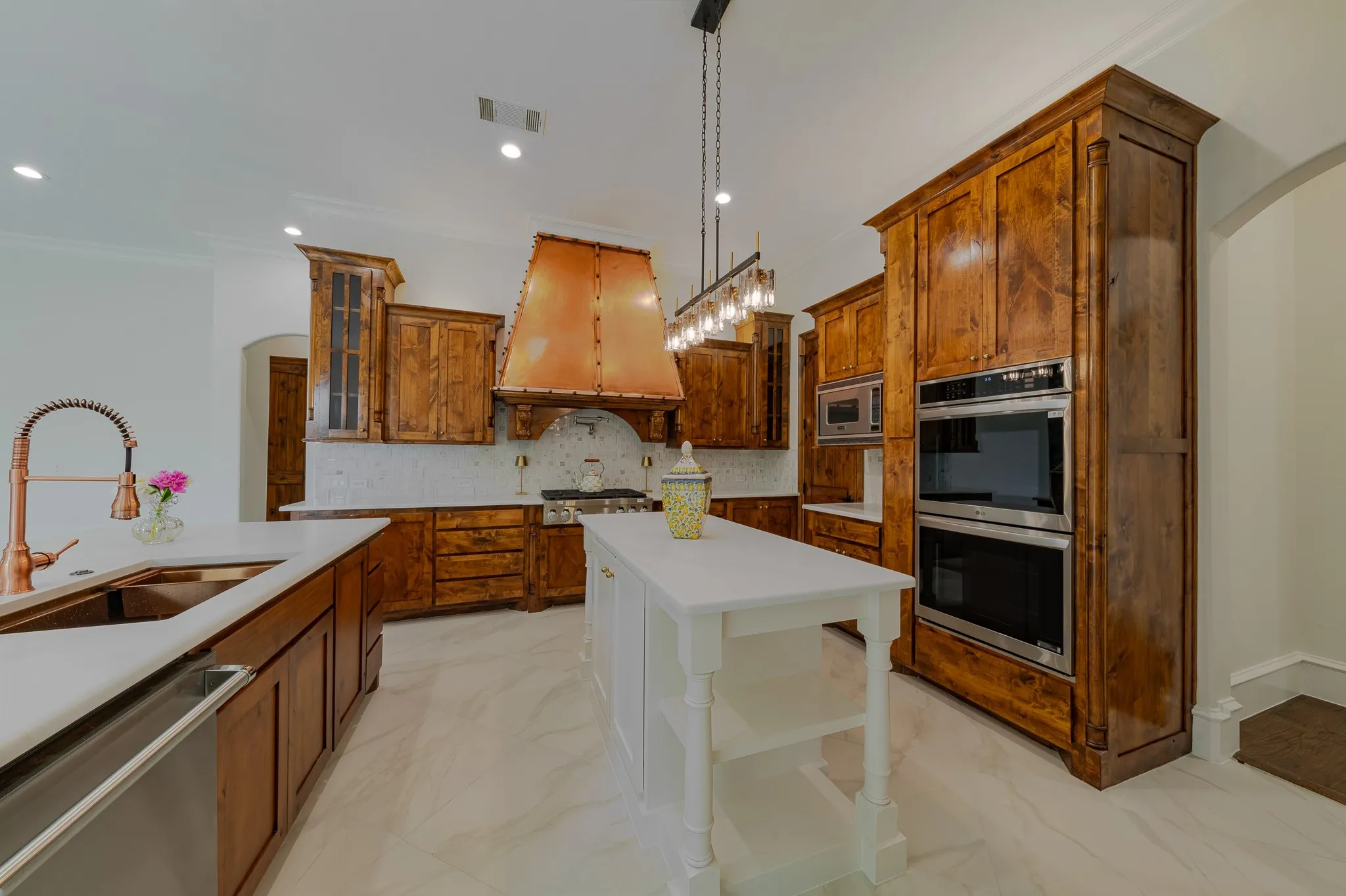Gourmet kitchen featuring custom wood cabinetry, stainless steel double ovens, and a striking copper range hood