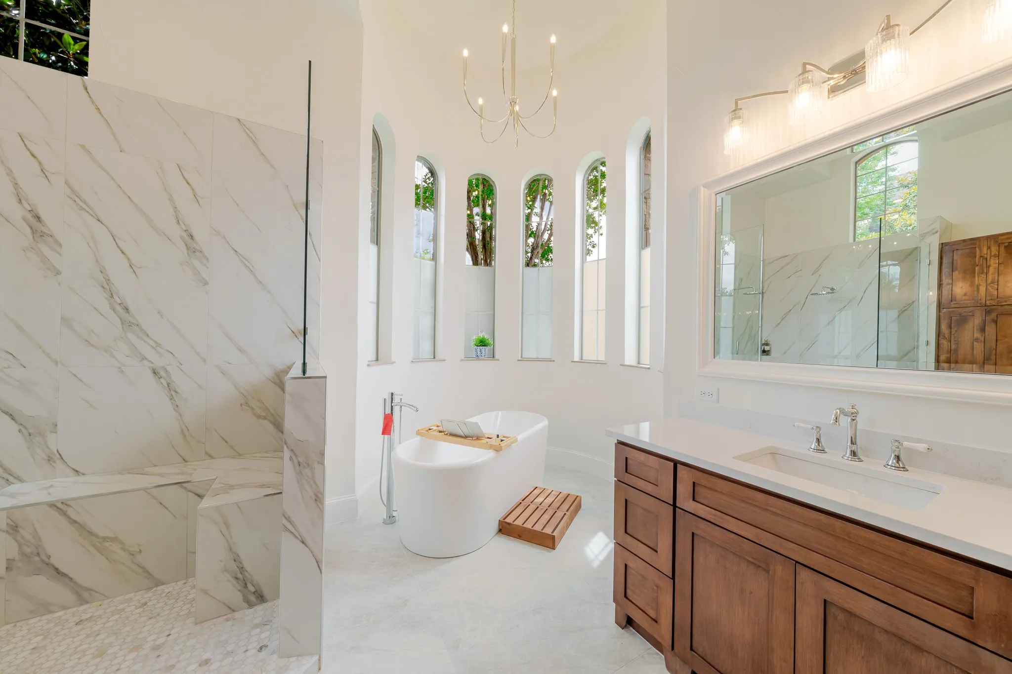 Freestanding soaking tub with a chandelier overhead and arched windows