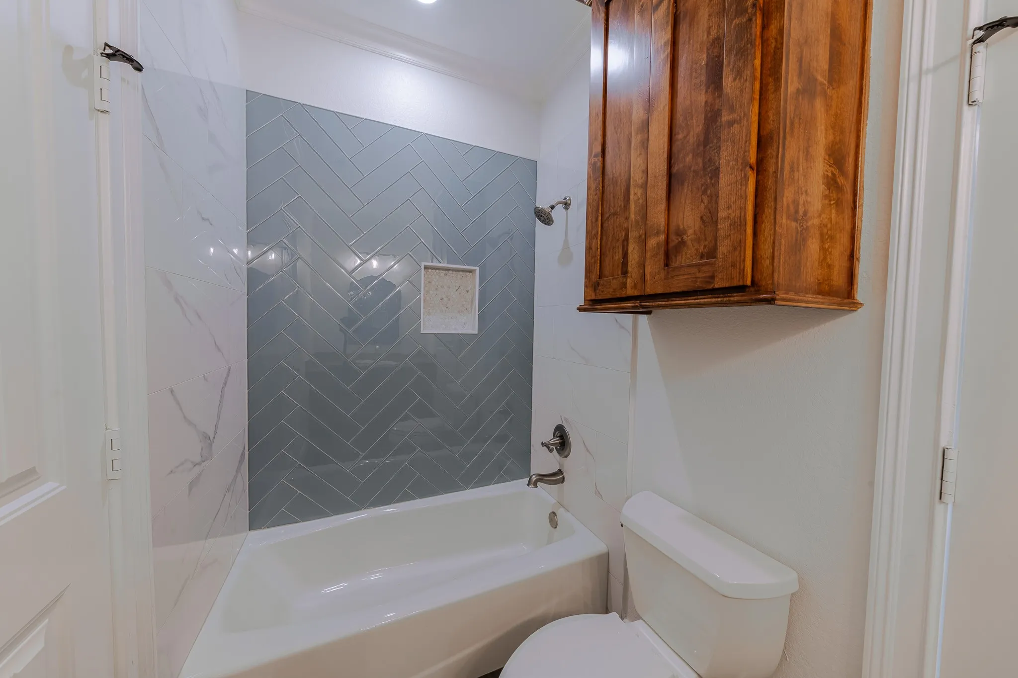 Bathtub with a herringbone tile surround in a contrasting grey hue and a built-in niche
