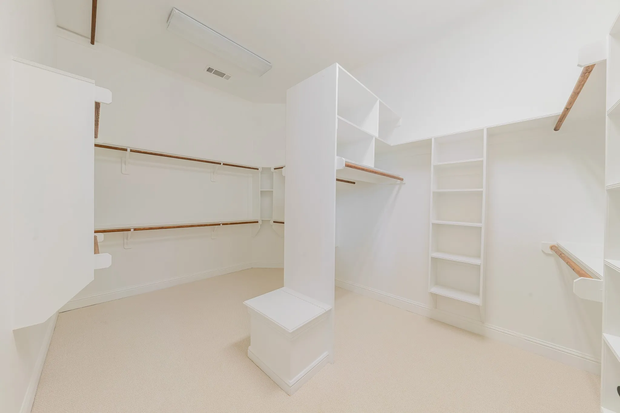 Spacious walk-in closet featuring built-in shelving, multiple hanging rods, and a central storage island with a bench top