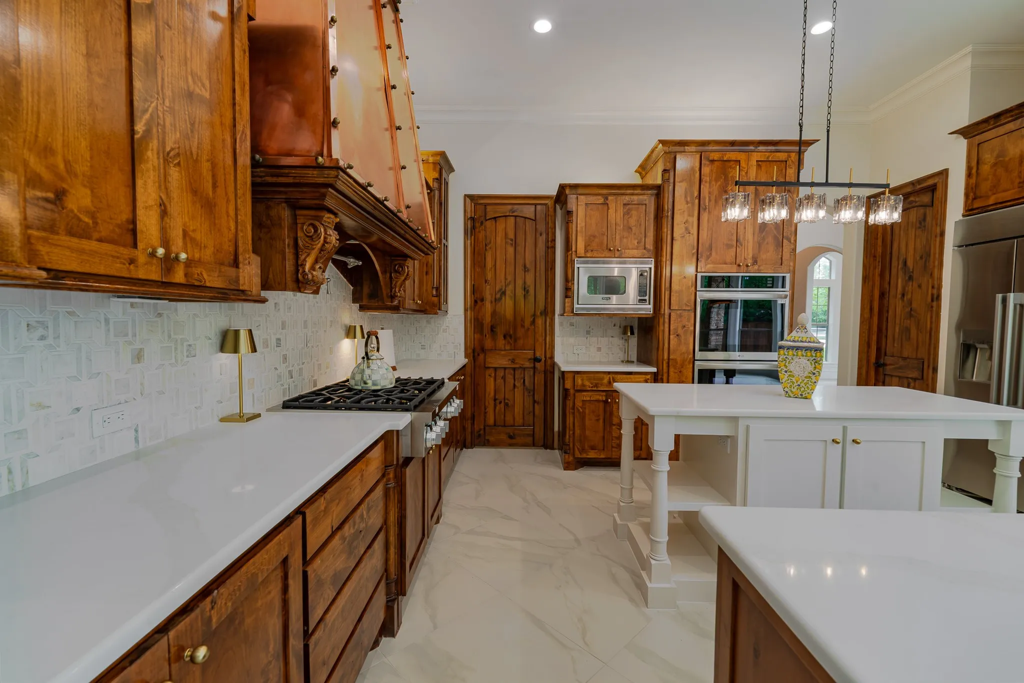 Gourmet kitchen featuring custom wood cabinetry, a decorative copper range hood, stainless steel appliances, and dual white kitchen islands with ample counter space