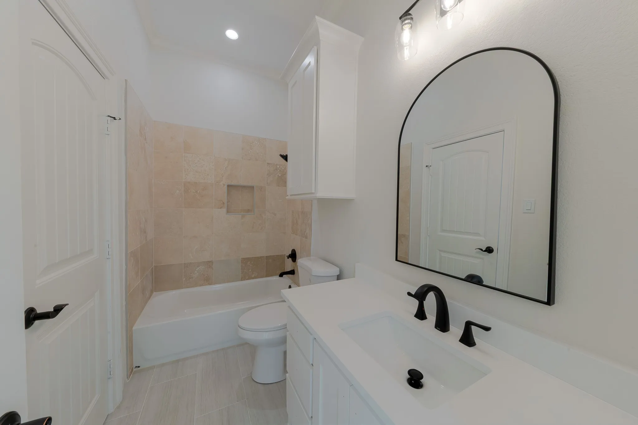 Bathroom featuring light-toned large format floor tiles, a white vanity with a solid surface countertop, and matte black plumbing fixtures