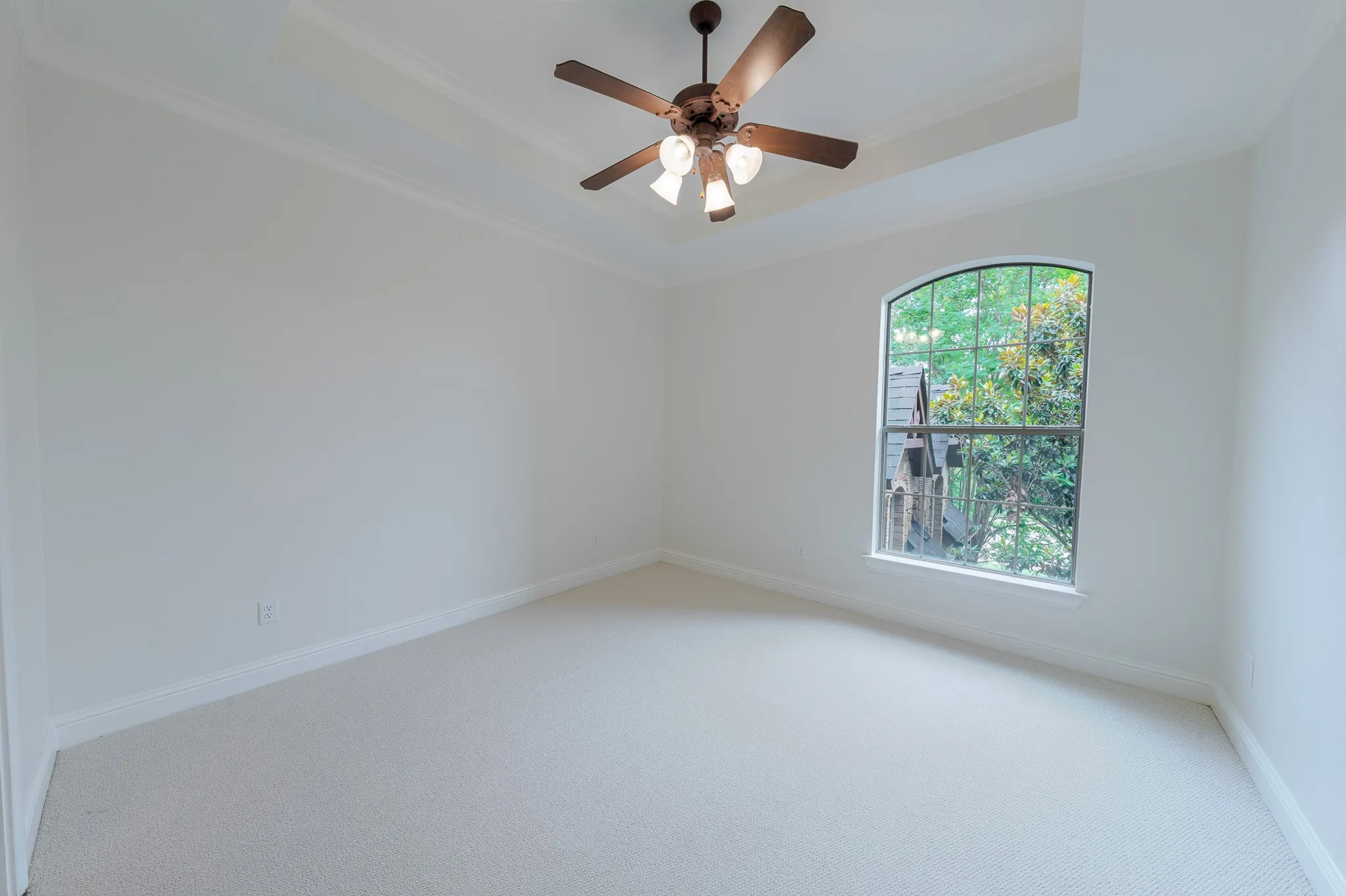 Arched window providing natural illumination, complemented by a tray ceiling and crown molding