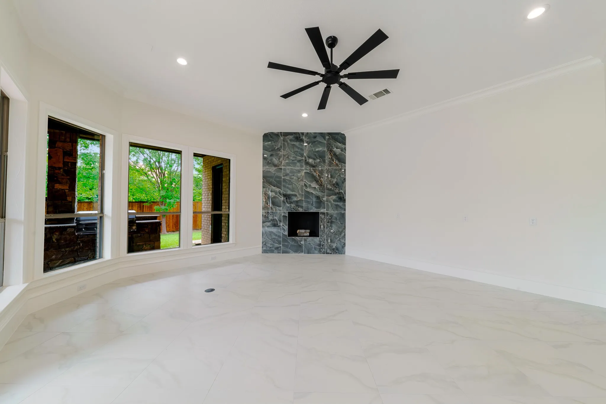 Spacious room featuring large format tile flooring, a dark stone-clad fireplace, and a contemporary ceiling fan