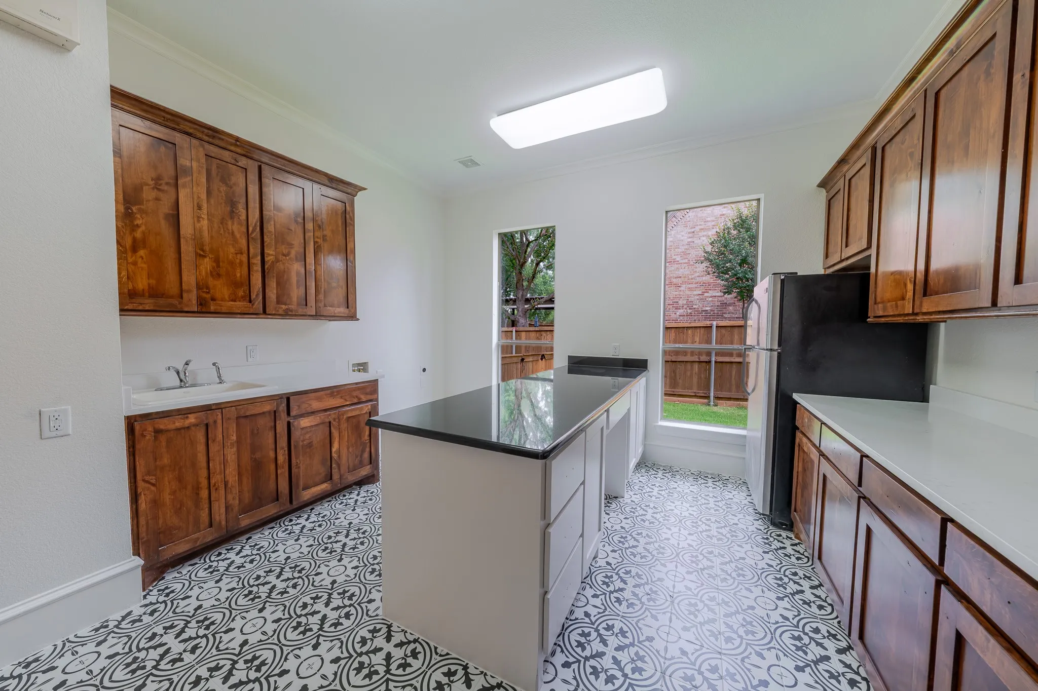 Kitchen or utility room featuring pattern-tiled flooring, wood cabinetry, a central island with a dark countertop, white perimeter countertops, and built-in sink