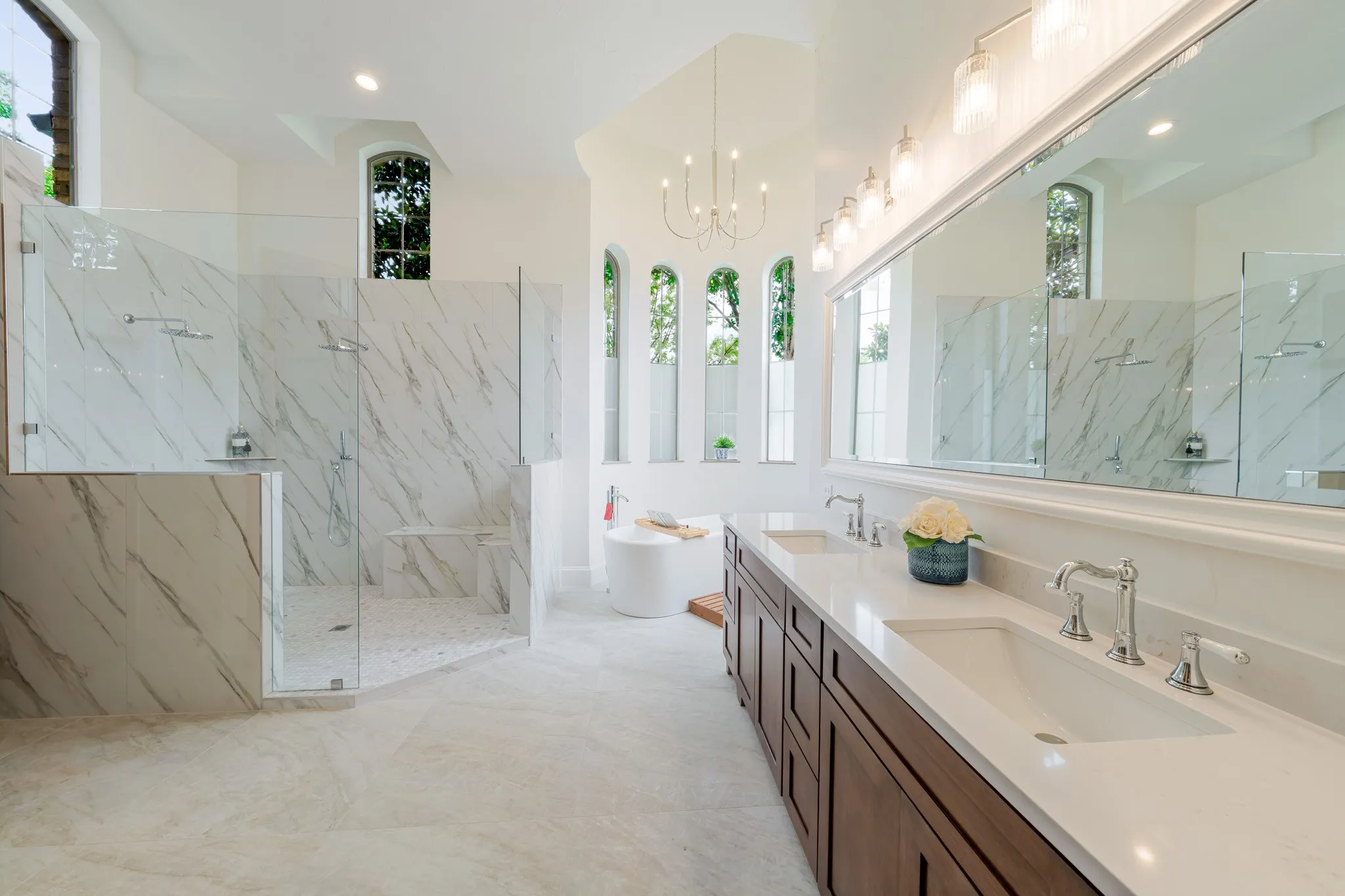 Spacious bathroom featuring a dual vanity with undermount sinks and chrome fixtures, a freestanding soaking tub, and a large walk-in shower with multiple showerheads and a built-in bench