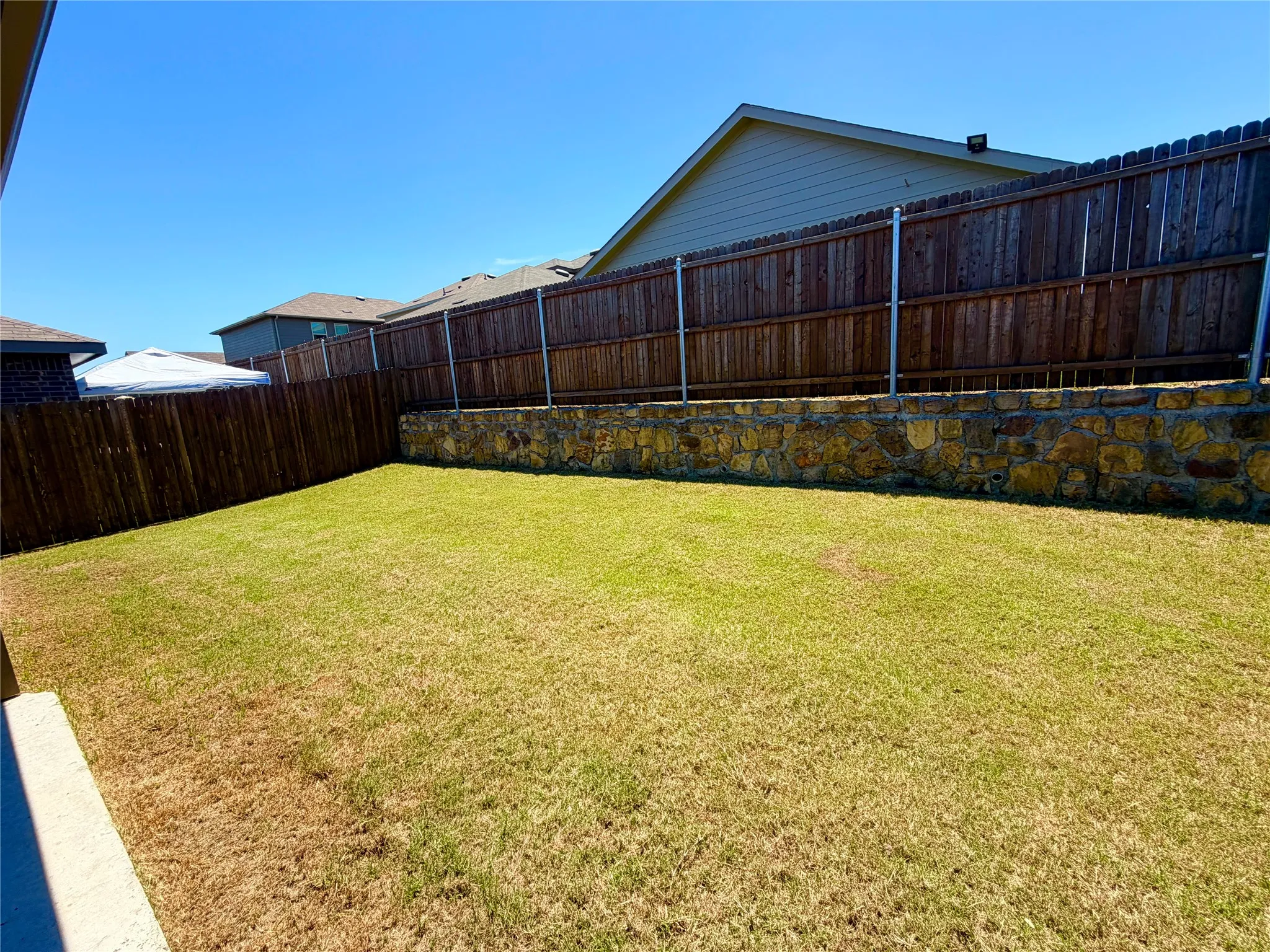 Spacious backyard featuring a stone retaining wall, wood fencing, and a large grass lawn