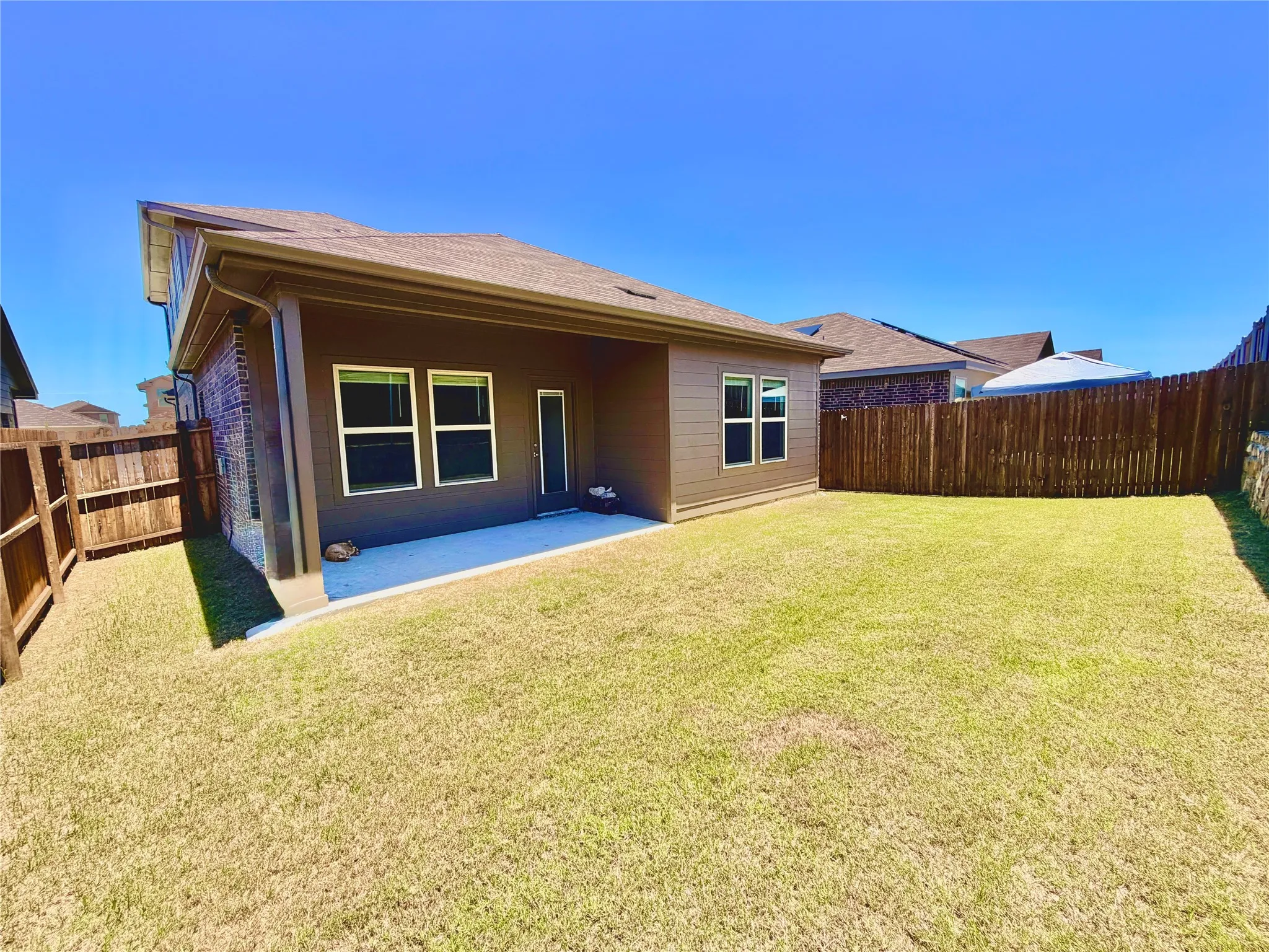 Expansive backyard featuring a concrete patio, wood fencing, and a stucco and brick exterior