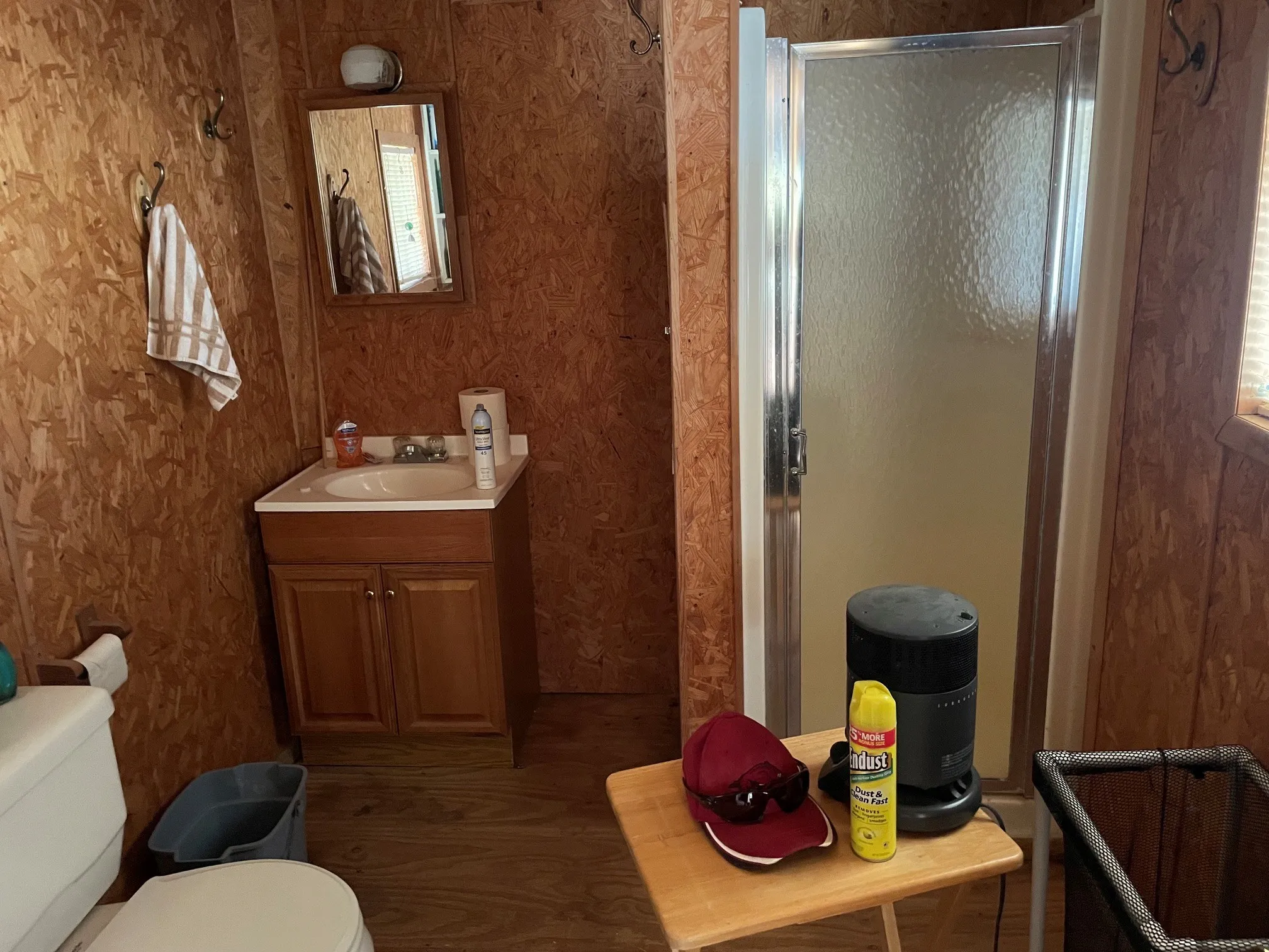 Bathroom featuring a wood-finish floor and walls, a vanity with a base cabinet, a toilet, a framed mirror, and a shower enclosure