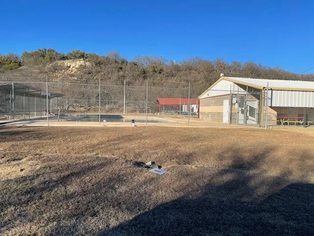 Outdoor recreation area featuring a fenced pool, a covered picnic area, and a large open field