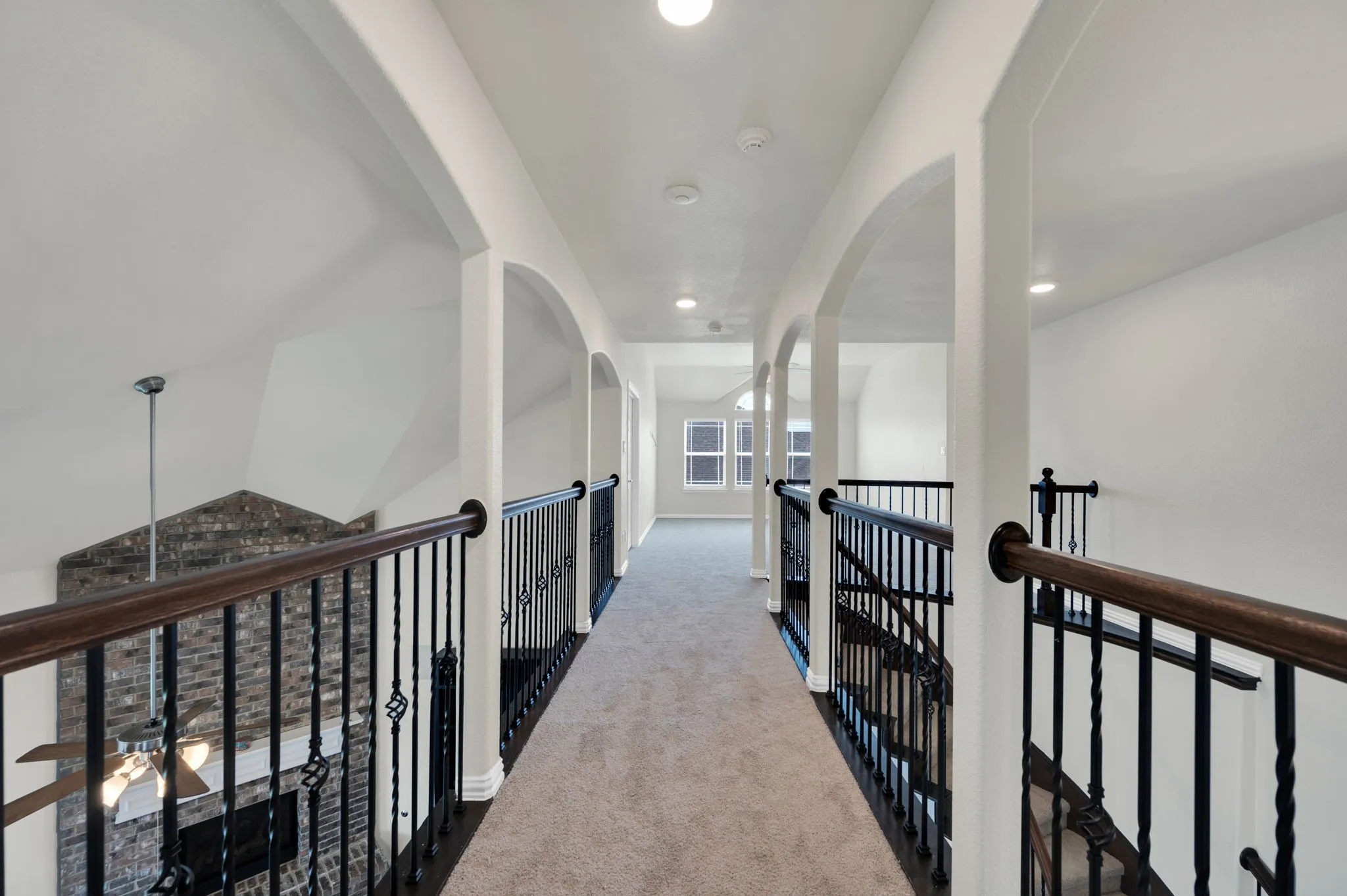 Carpeted second-story hallway with arched entryways, recessed lighting, and a dark wood-finish handrail with wrought iron balusters