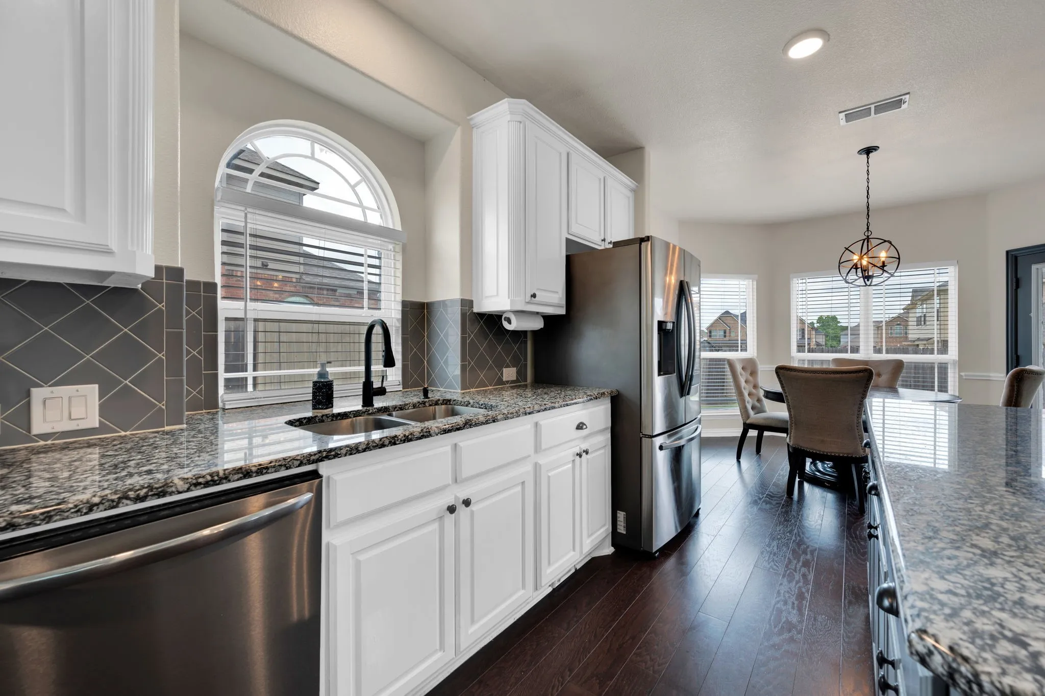 Bright kitchen featuring white cabinetry, granite countertops, a diamond-patterned tile backsplash, a stainless steel dishwasher, and a deep double sink with a black fixture