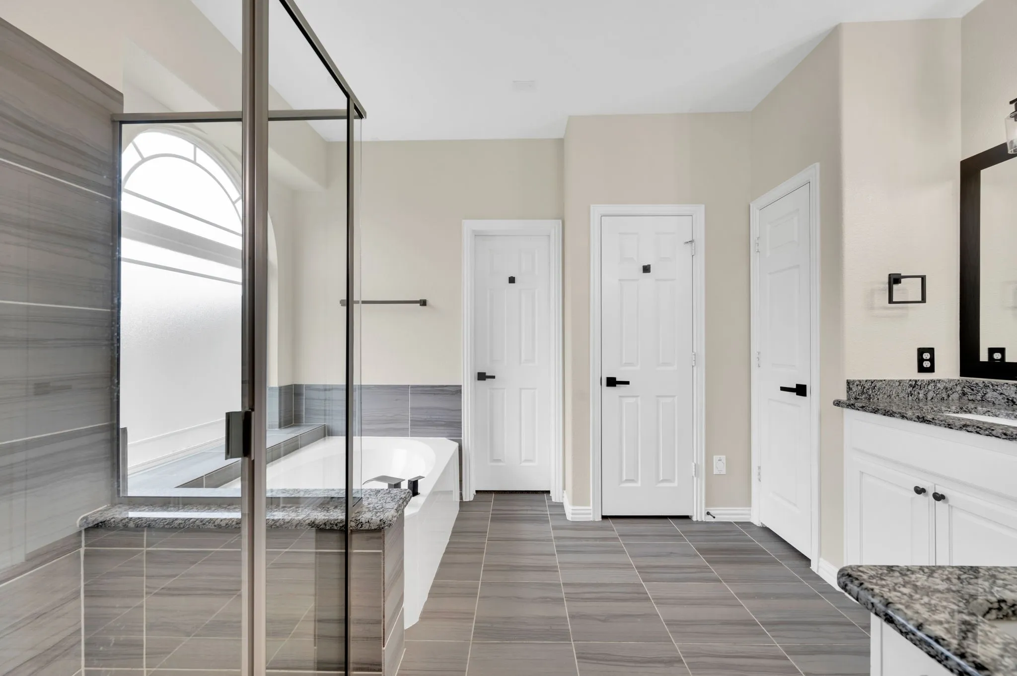 Contemporary bathroom featuring a spacious walk-in shower with a frameless glass enclosure, a built-in soaking tub, a granite-topped vanity with white cabinetry, and large format tile flooring