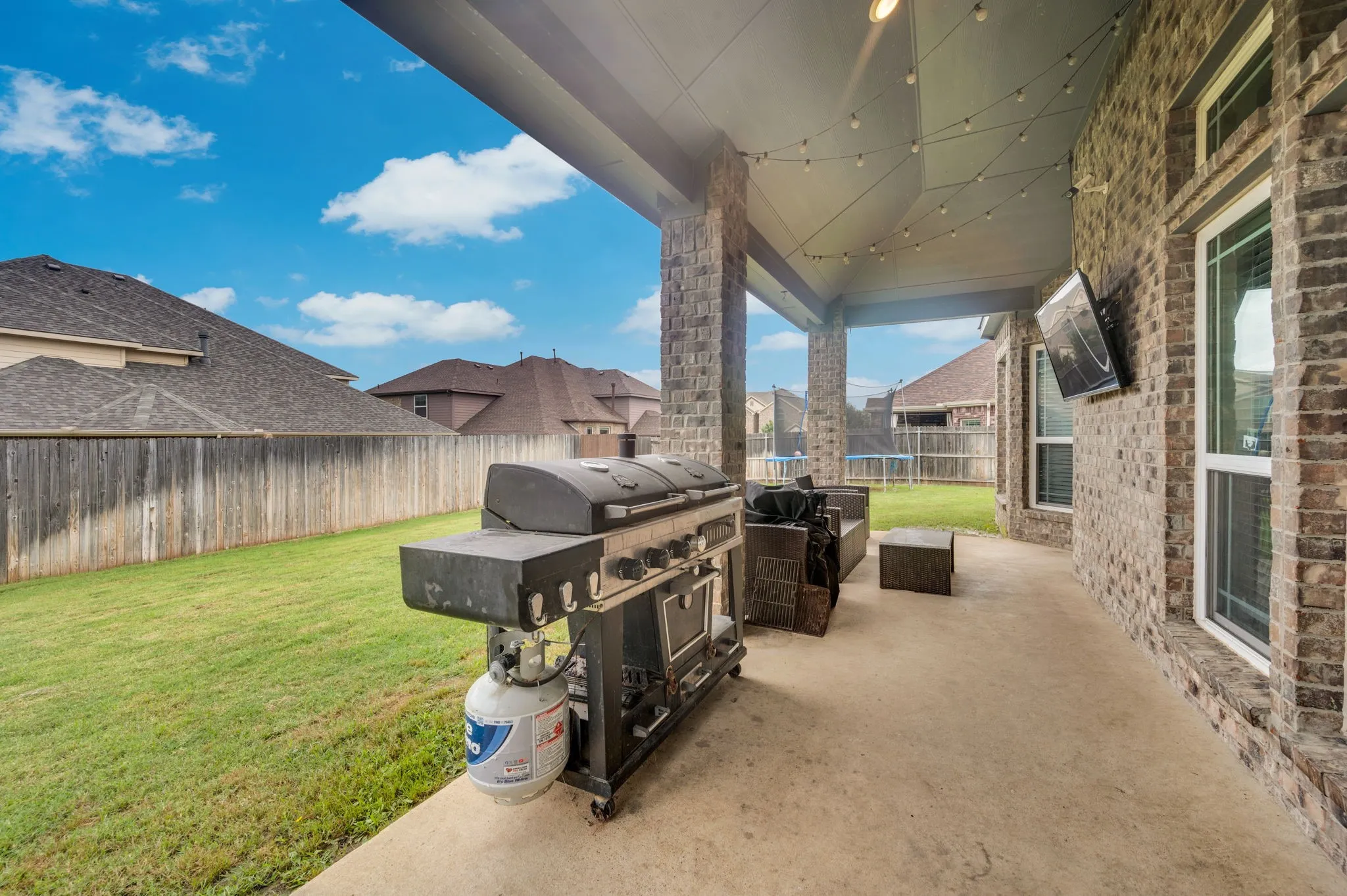 Expansive covered patio featuring a concrete surface, brick columns, and string lighting