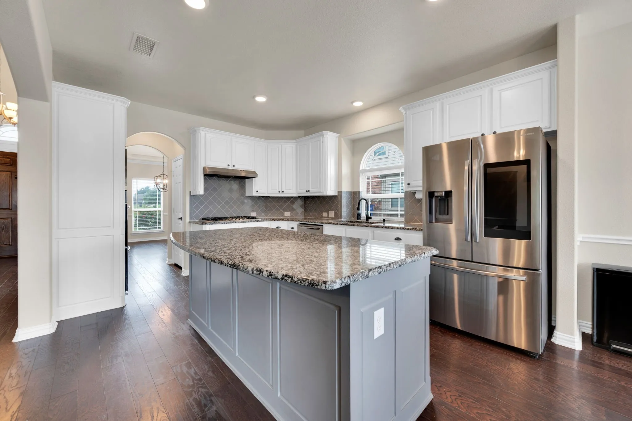 Gourmet kitchen featuring a large island with granite countertop, white cabinetry, dark wood-finish flooring, stainless steel French door refrigerator, and a diamond-patterned backsplash