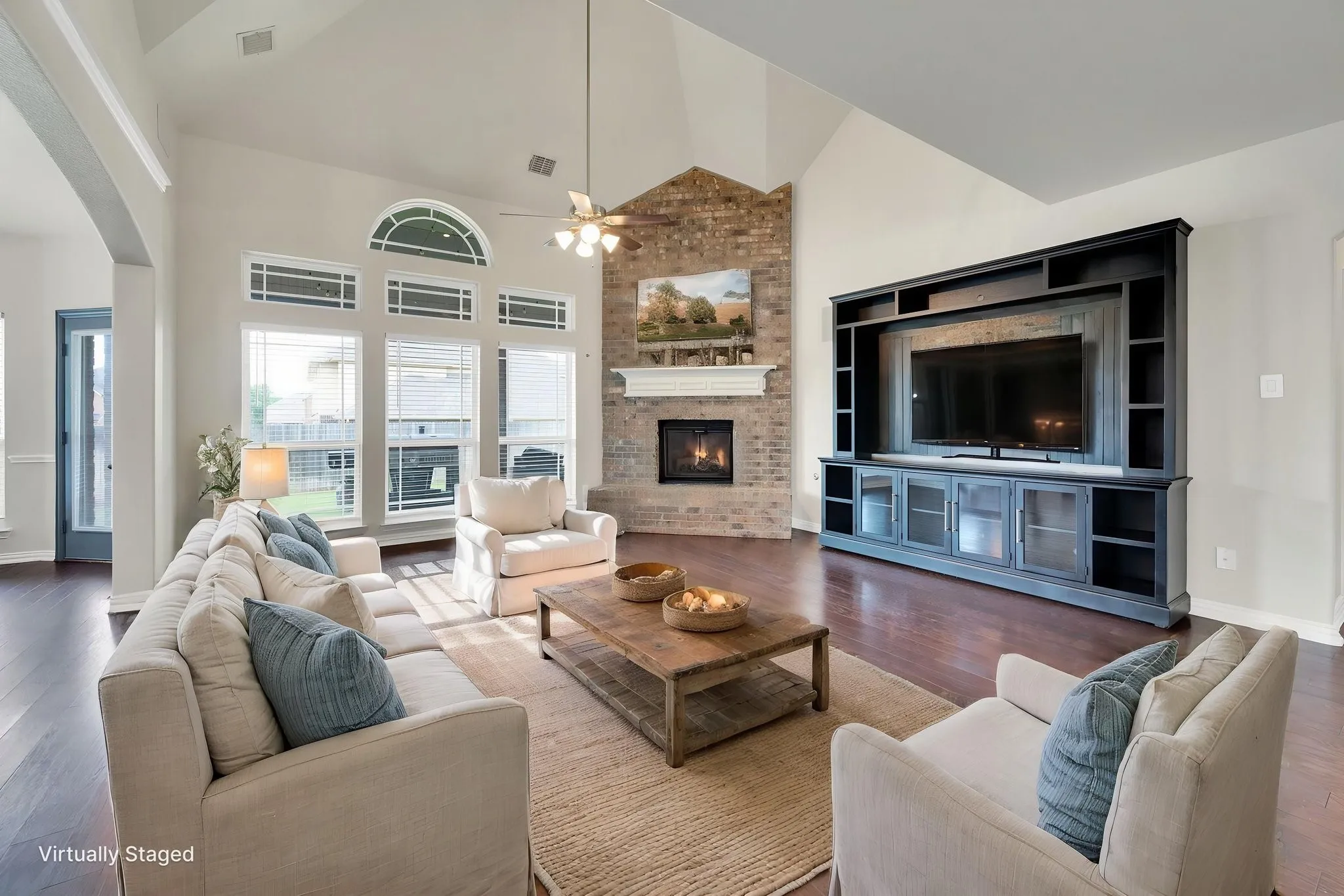 Vaulted ceiling living area featuring dark wood-finish flooring, a brick-surround fireplace with a white mantel, and a built-in media center