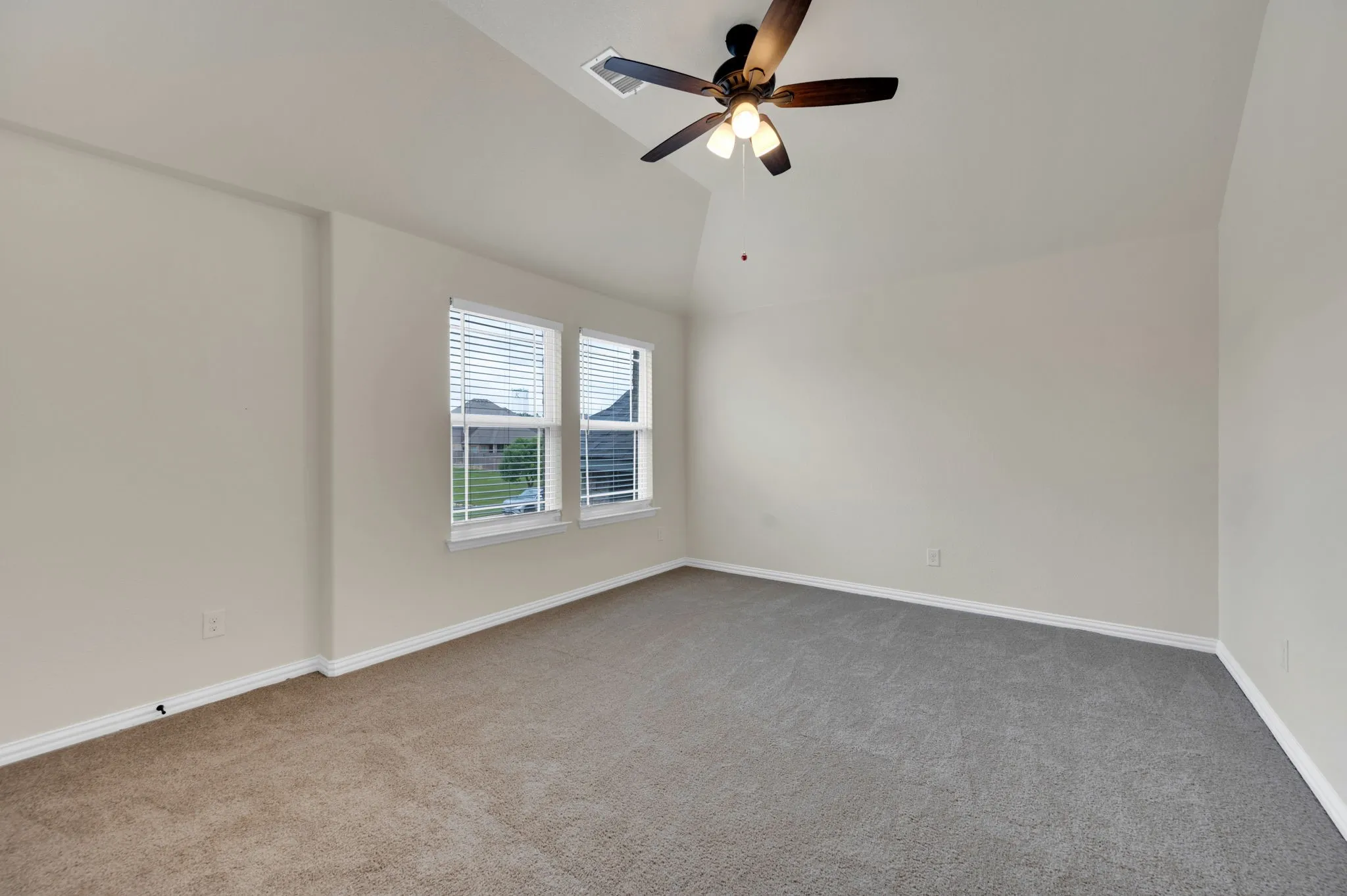 Carpeted room featuring a vaulted ceiling with a ceiling fan, two windows with blinds, and light-colored walls
