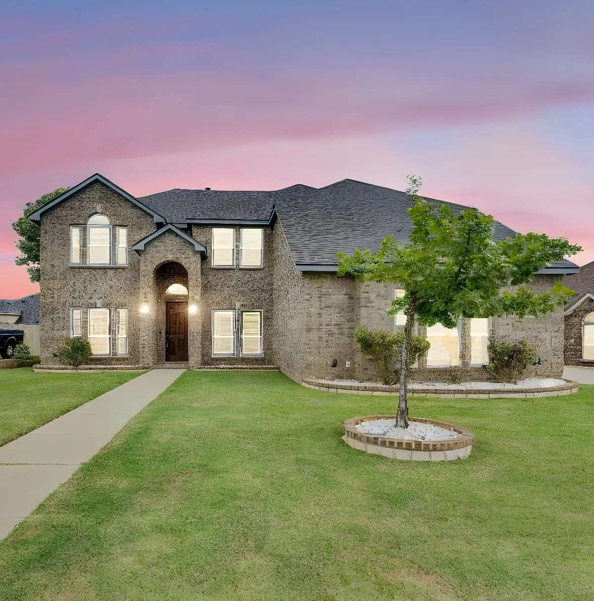 Brick exterior home with a dark shingle roof, arched entryway, and multiple windows