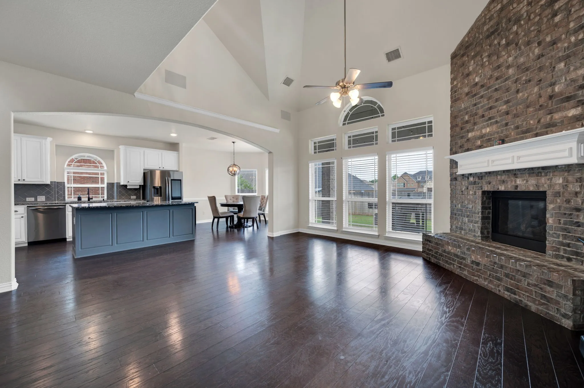 Open-concept living space featuring wood-finish flooring, a vaulted ceiling, and a brick fireplace with a white mantel
