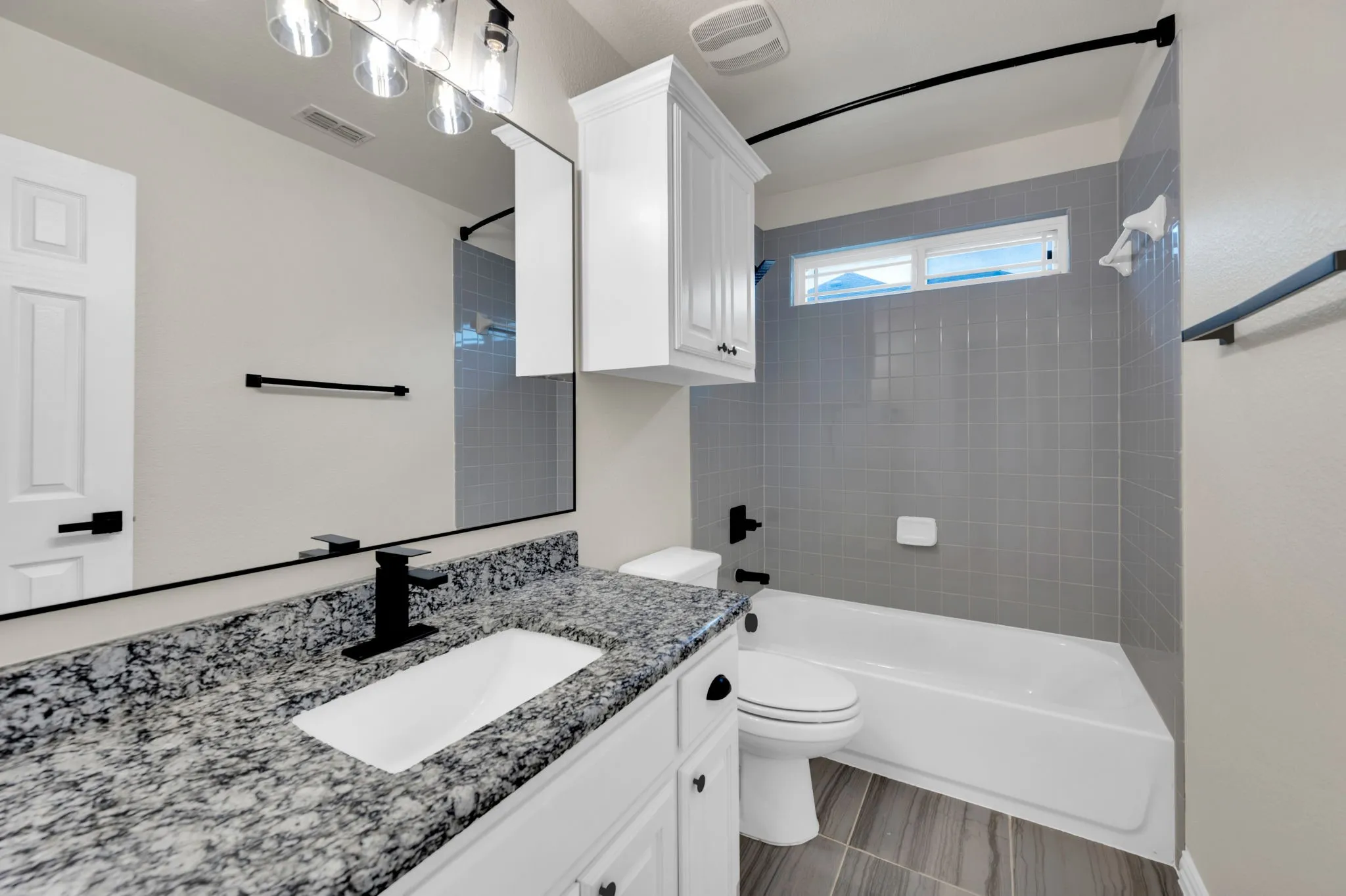 Bathroom featuring a granite countertop vanity with an undermount sink and matte black faucet, a white bathtub with subway tile surround, white cabinetry, and wood-look floor tiles