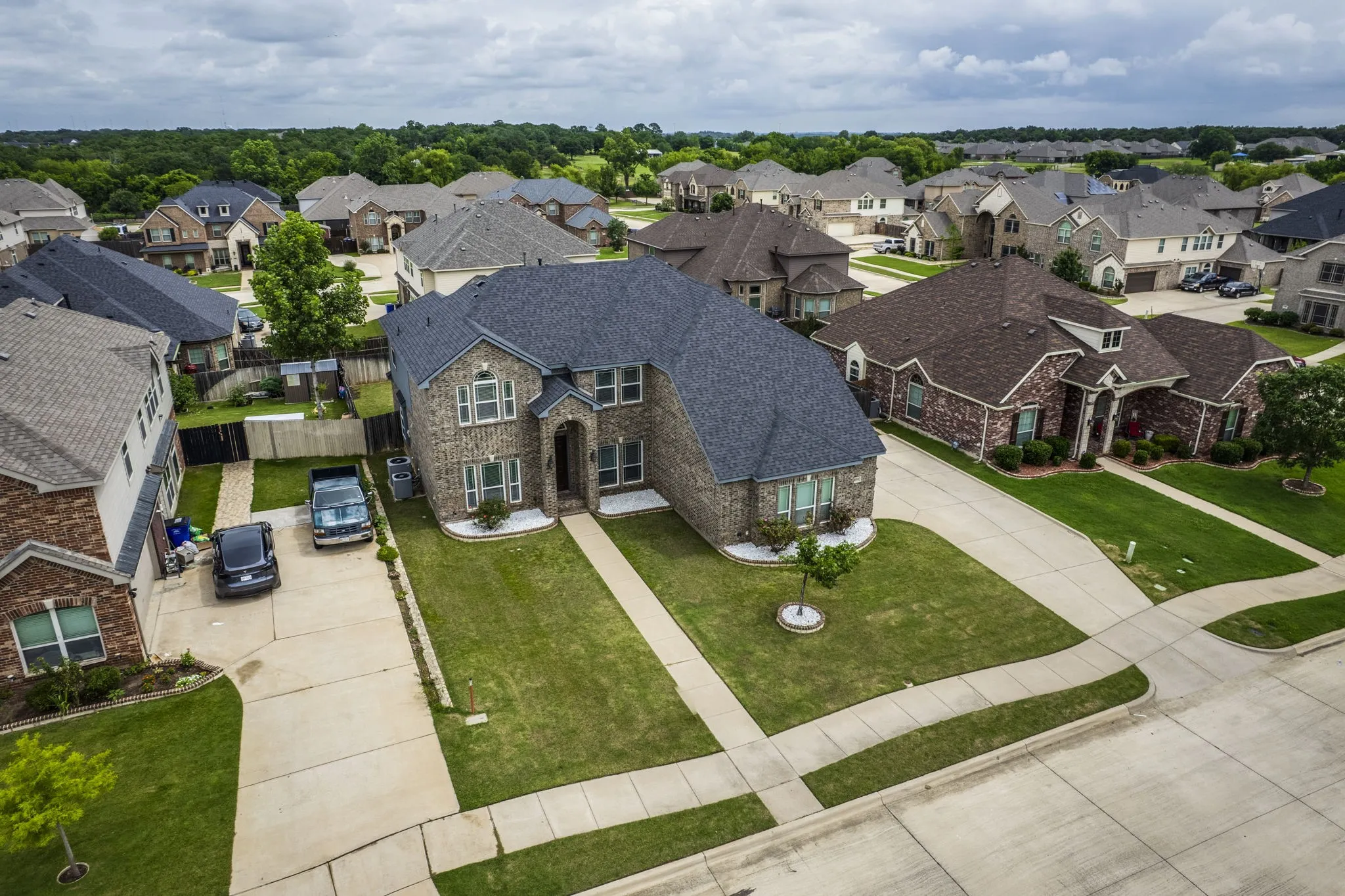 Brick facade residence featuring a dark shingle roof and a landscaped front lawn