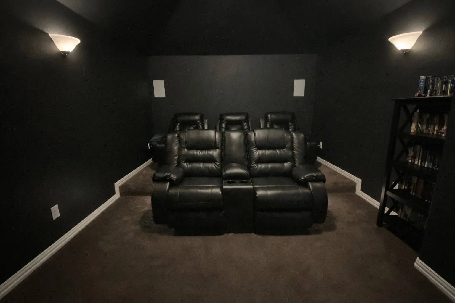 Dedicated media room featuring tiered seating, dark-toned walls, and recessed wall speakers