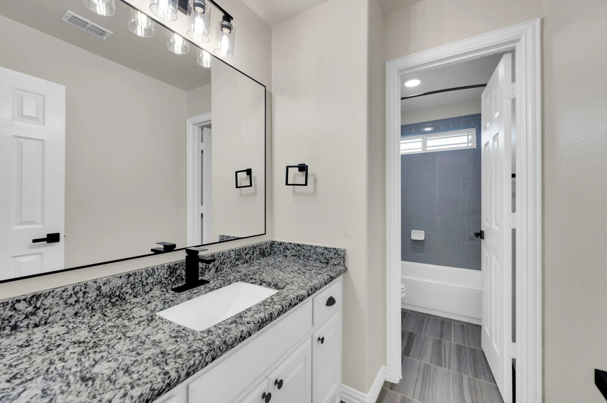 Bathroom vanity featuring a rectangular undermount sink, black faucet, and speckled countertop