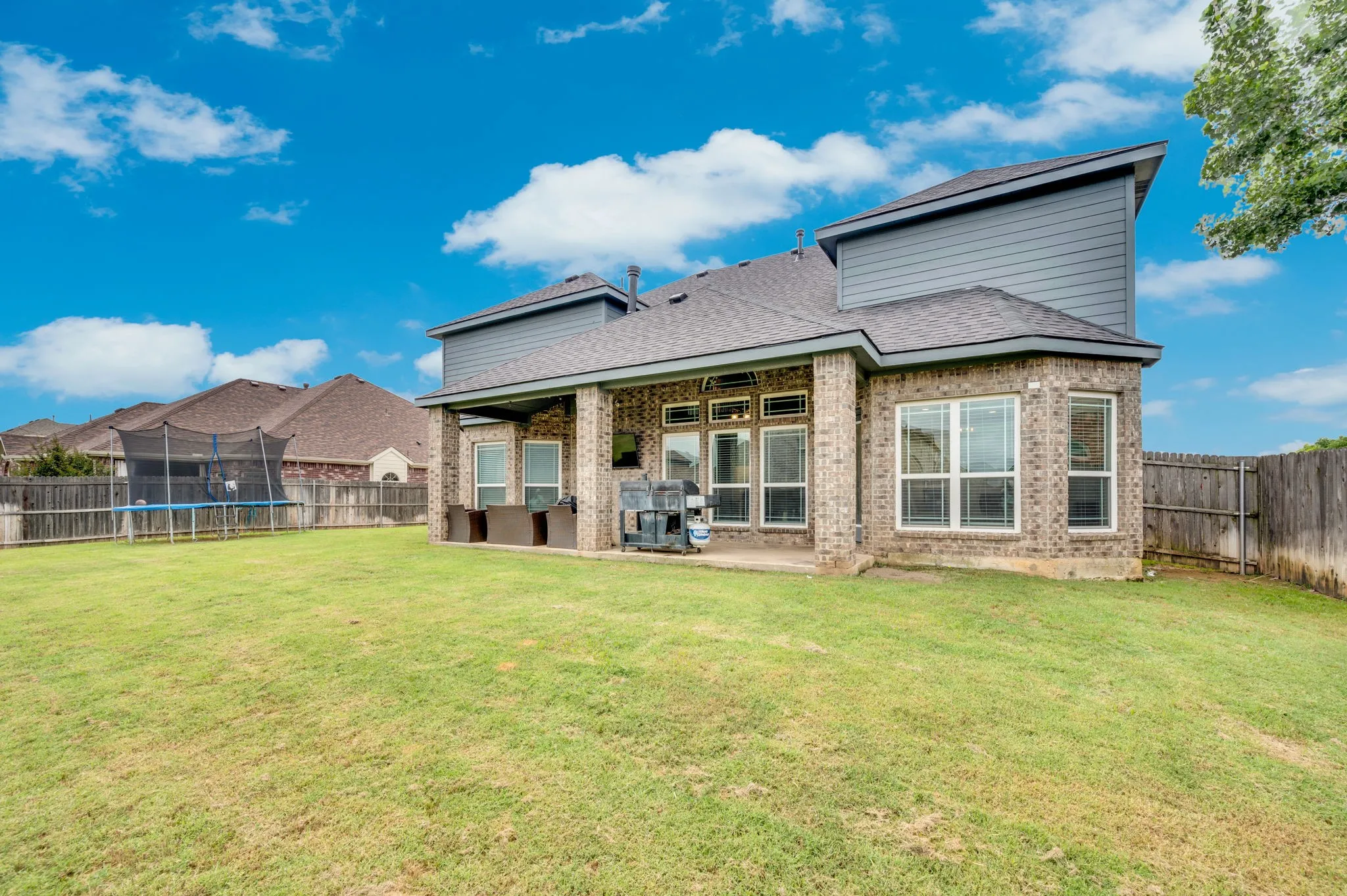 Expansive green lawn with a covered patio, brick exterior, and multiple large windows