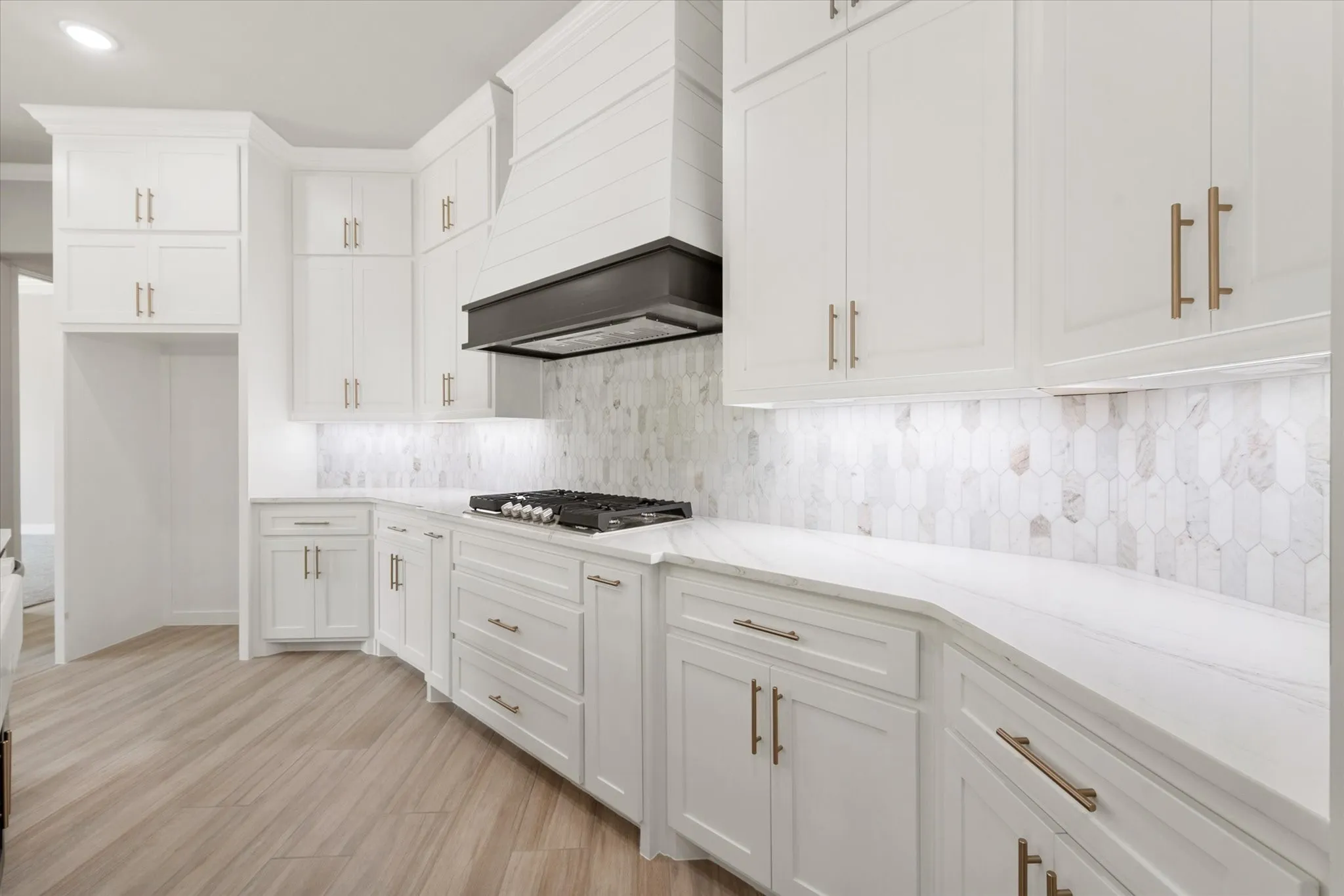 Modern kitchen featuring white cabinetry with gold-finish hardware, a gas cooktop, and a white pick-tile backsplash