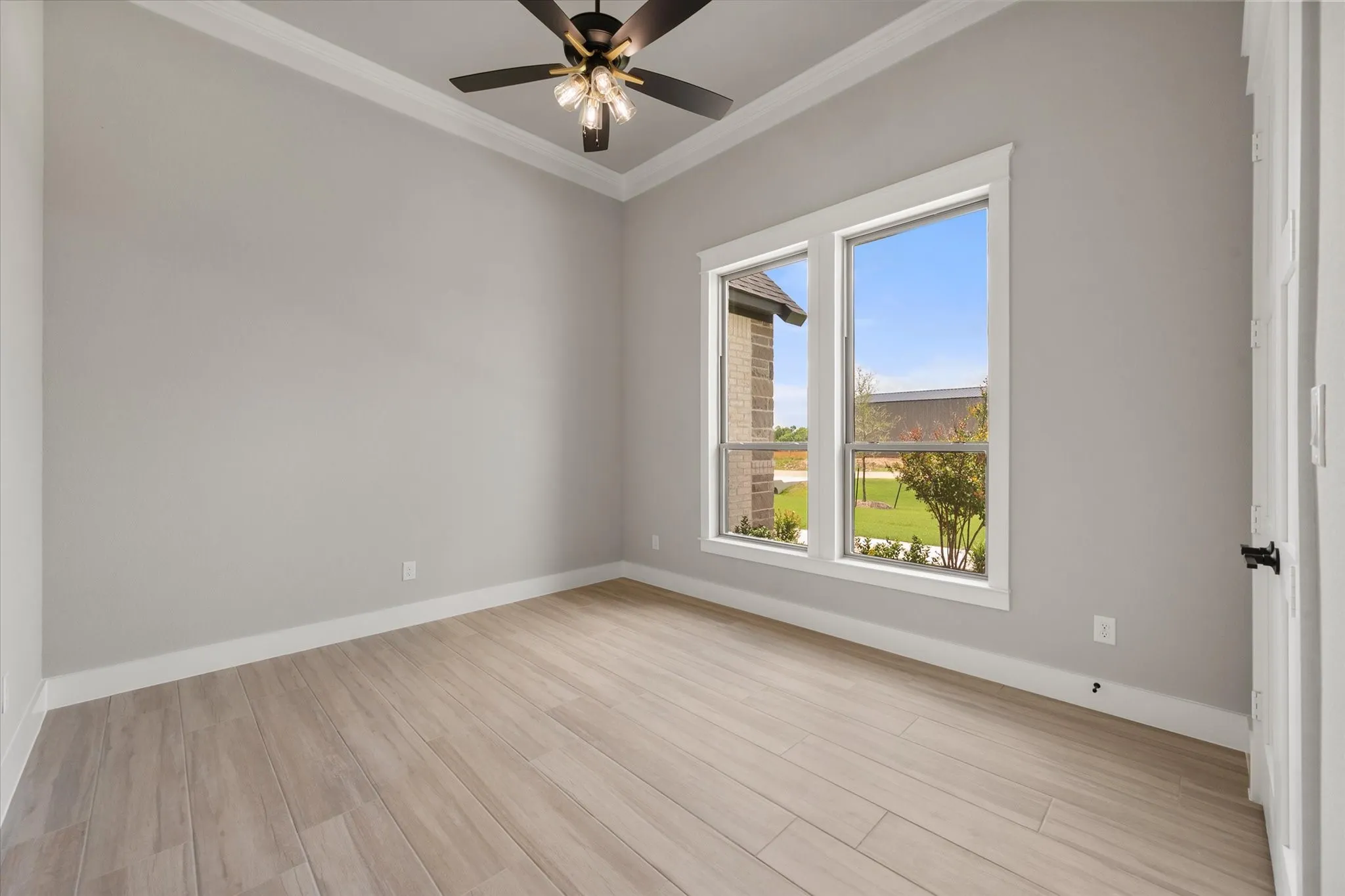 Room featuring wood-finish flooring, two large windows, a ceiling fan with integrated lighting, crown molding, and white baseboards