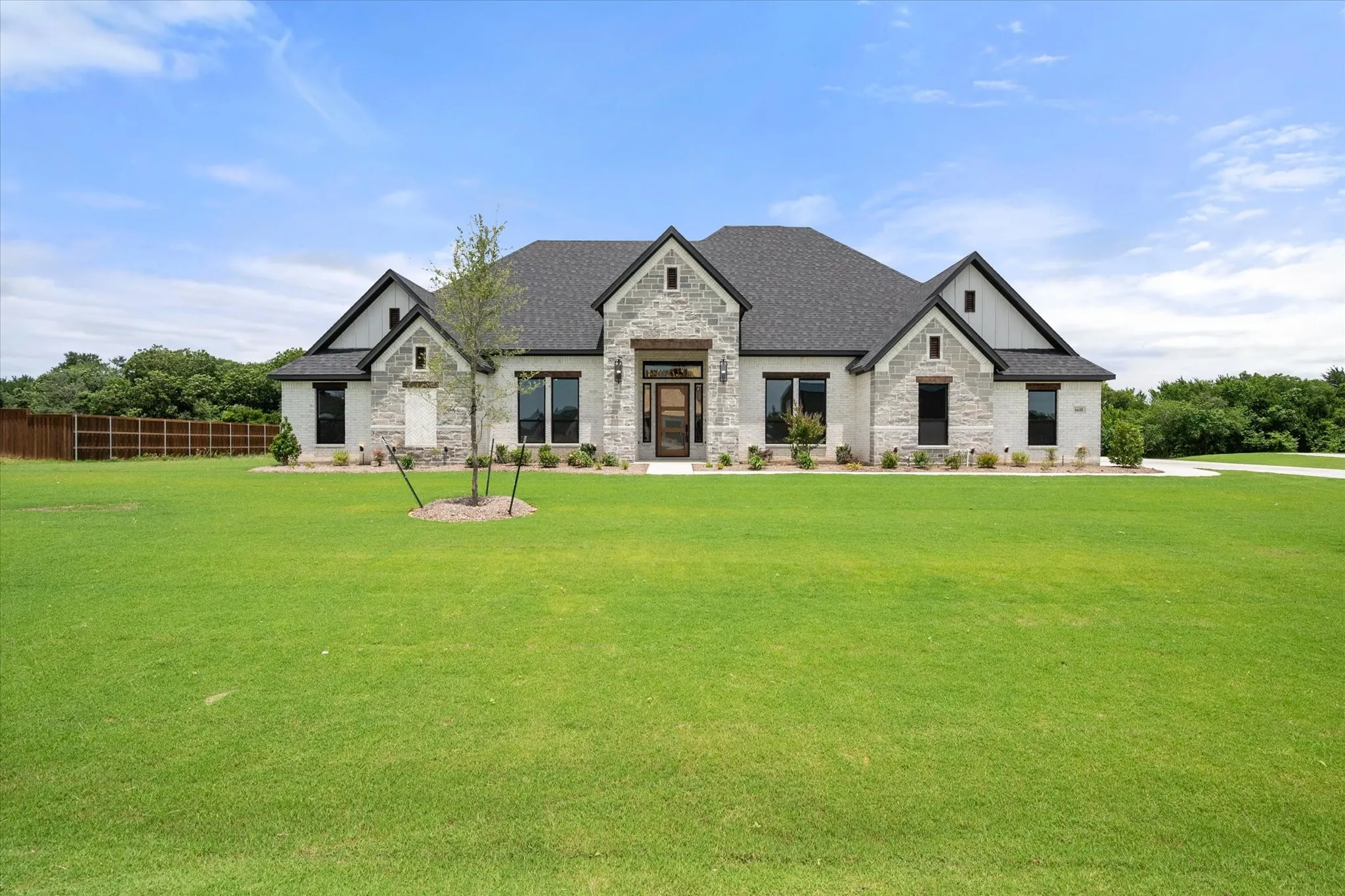 Contemporary single-story residence featuring a stone and board-and-batten facade, dark shingle roofing, and multiple large windows