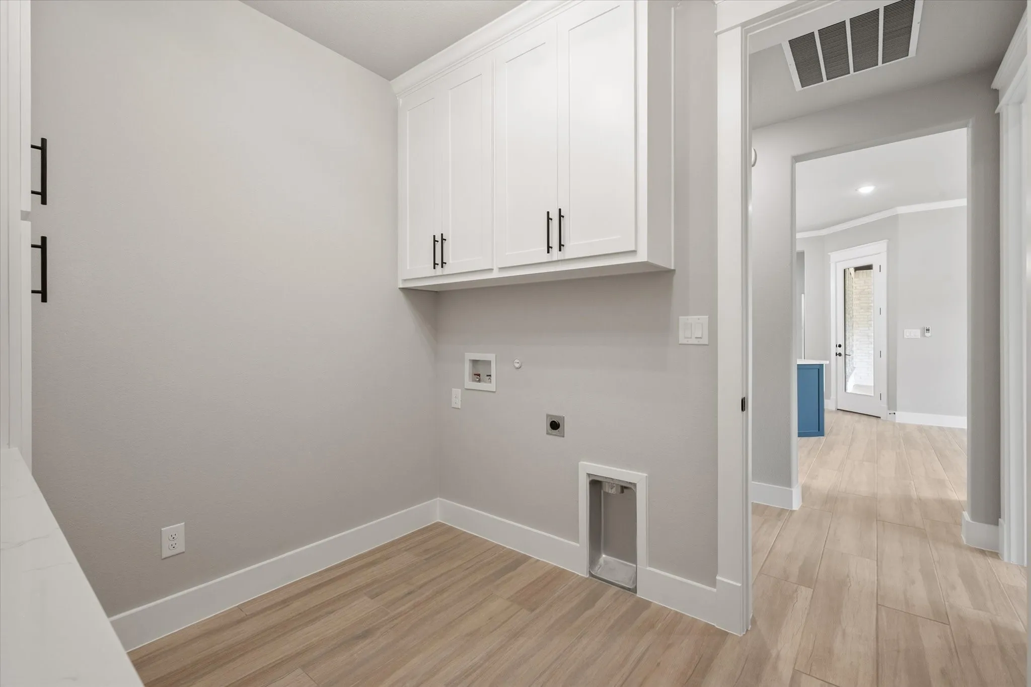 Laundry area featuring white shaker-style cabinetry with black hardware, light wood-finish flooring, and light gray walls