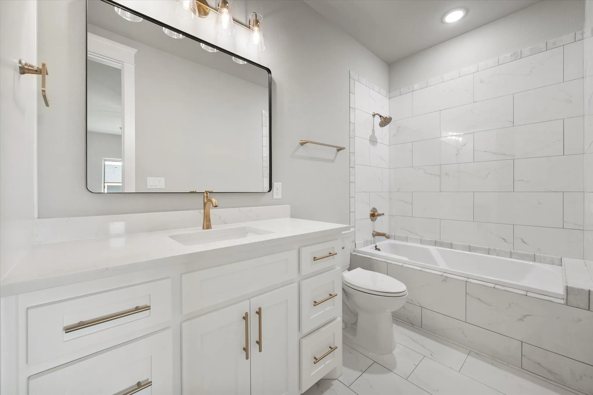 Modern bathroom featuring a white vanity with gold-finish hardware, a rectangular undermount sink, and a large black-framed mirror
