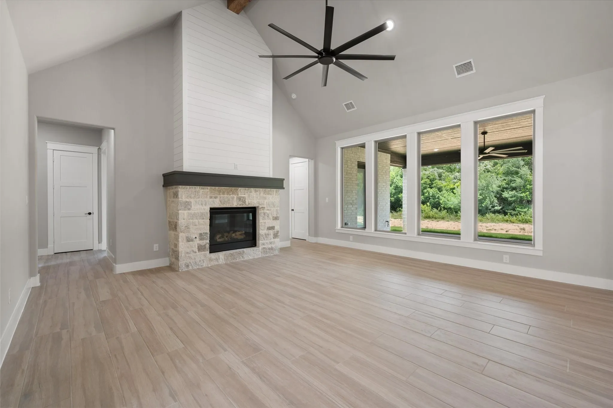 Spacious living area featuring a vaulted ceiling, wood-finish flooring, and a stone fireplace with a shiplap surround