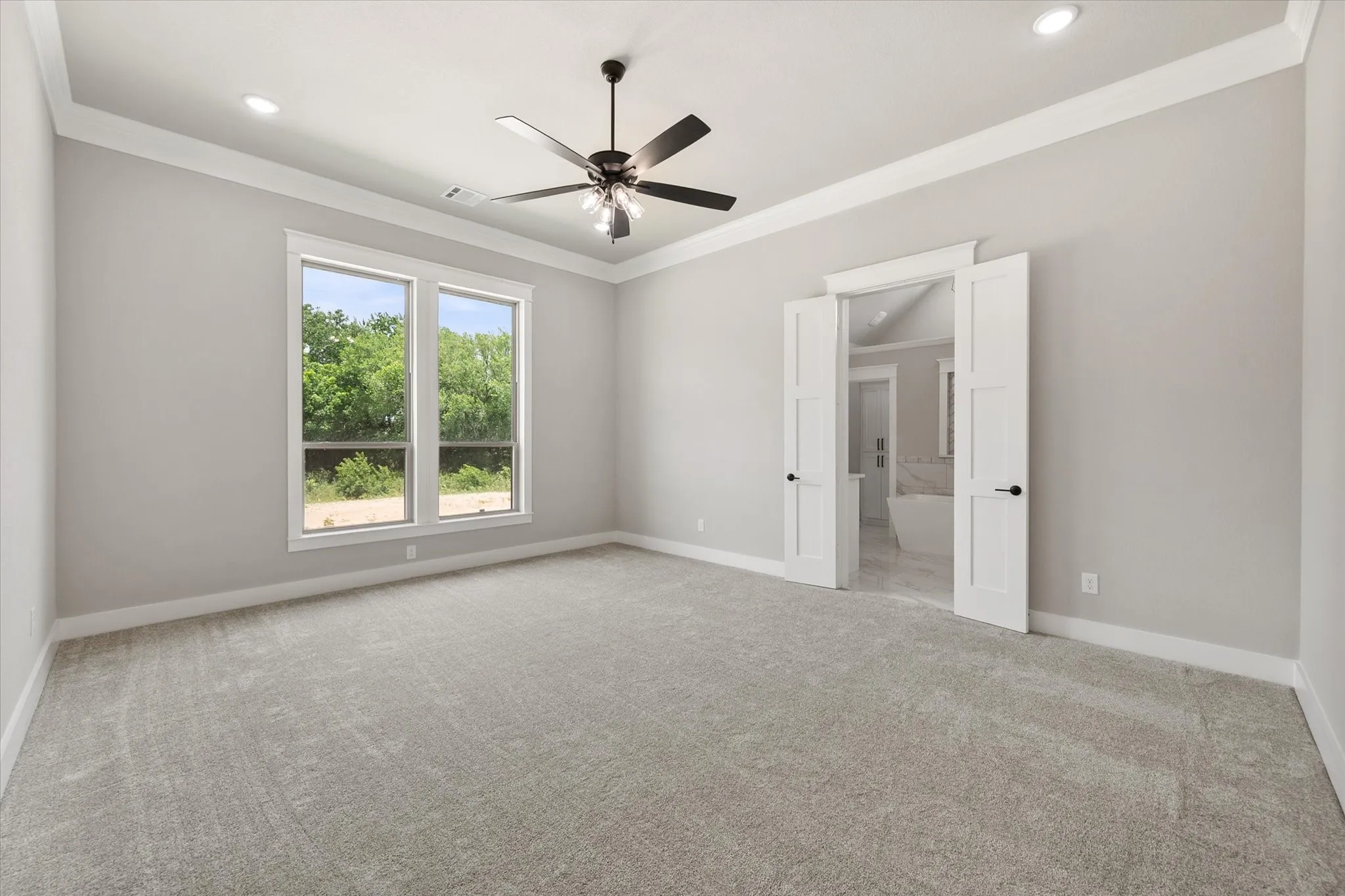 Spacious room featuring light gray carpet, multiple windows, a ceiling fan, recessed lighting, and crown molding