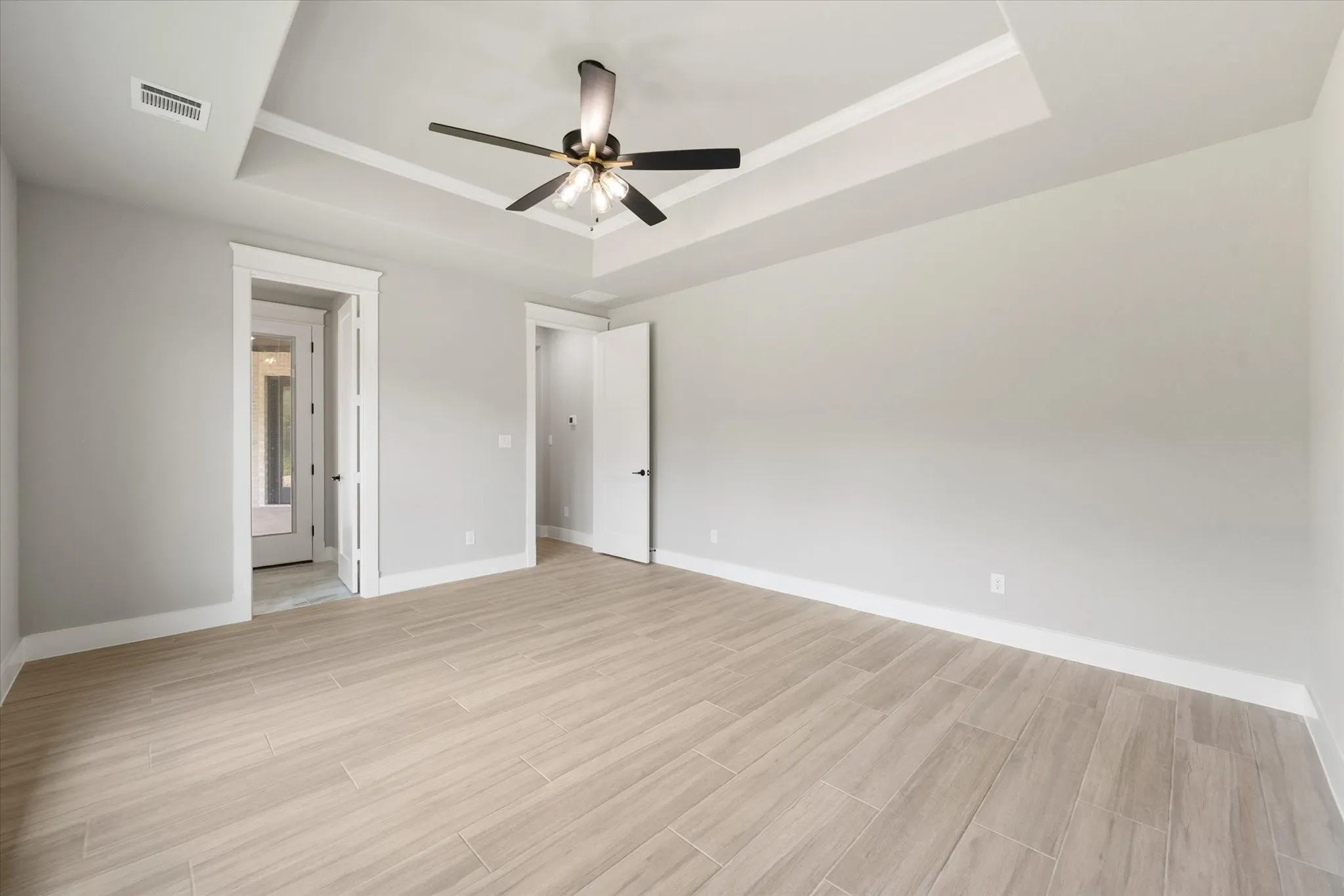 Spacious interior featuring wood-look tile flooring, light gray walls, a tray ceiling with crown molding, and a modern ceiling fan