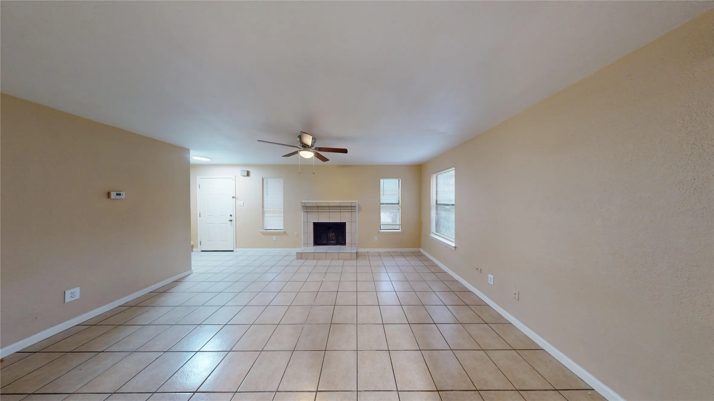 Spacious living area featuring tile flooring, a fireplace with a stone surround and hearth, multiple windows, and a ceiling fan