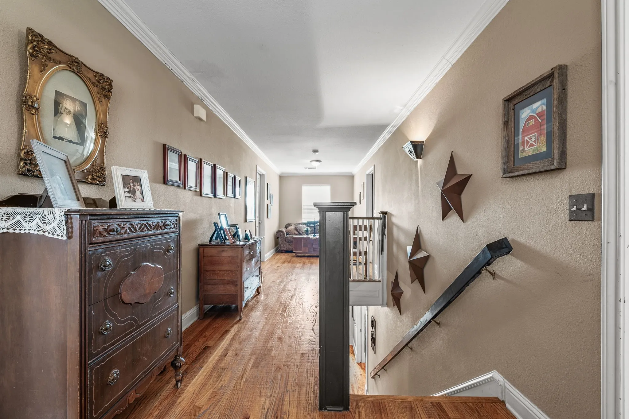 Hallway featuring wood-finish flooring, crown molding, neutral wall color, and a dark wood-finish staircase with coordinating handrail