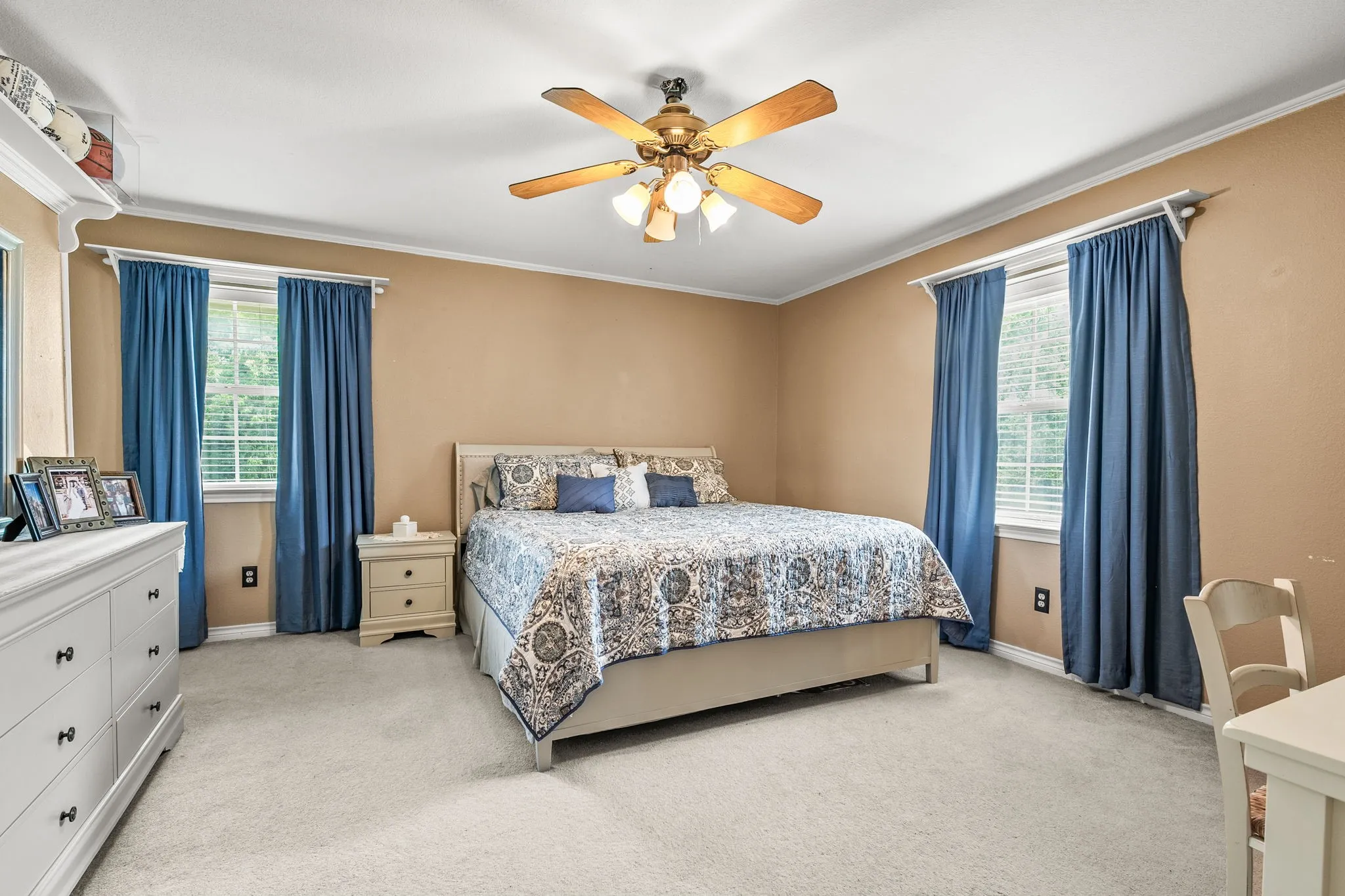 Carpeted bedroom featuring two windows with blinds, a ceiling fan with light fixture, and crown molding