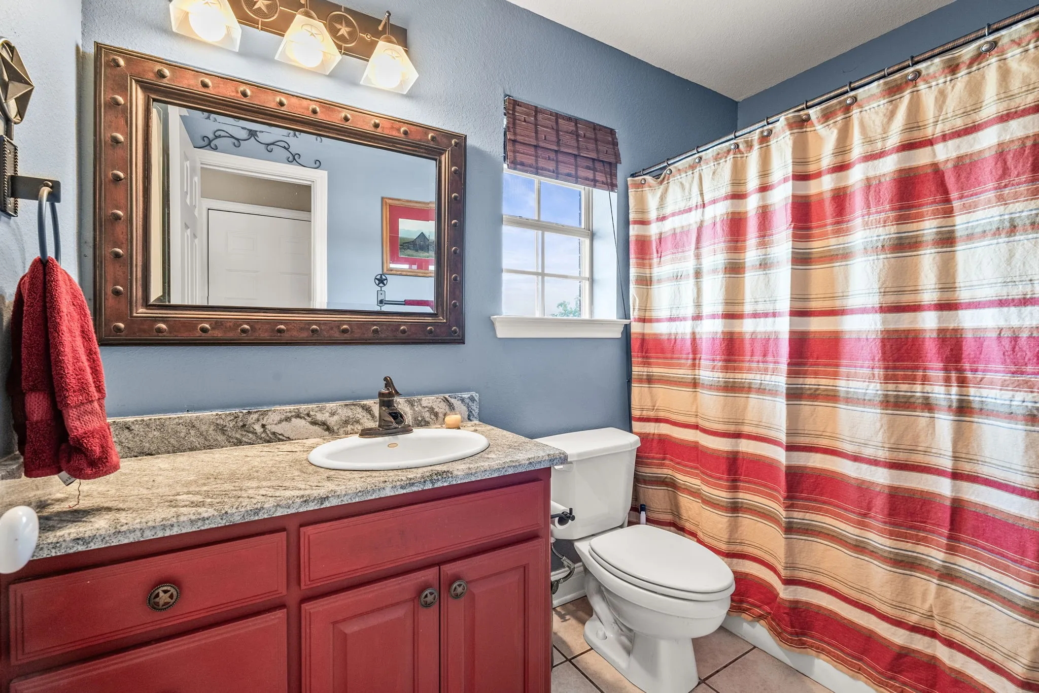 Bathroom featuring a vanity with a red wood-finish base, a light-colored speckled countertop, and an integrated white sink