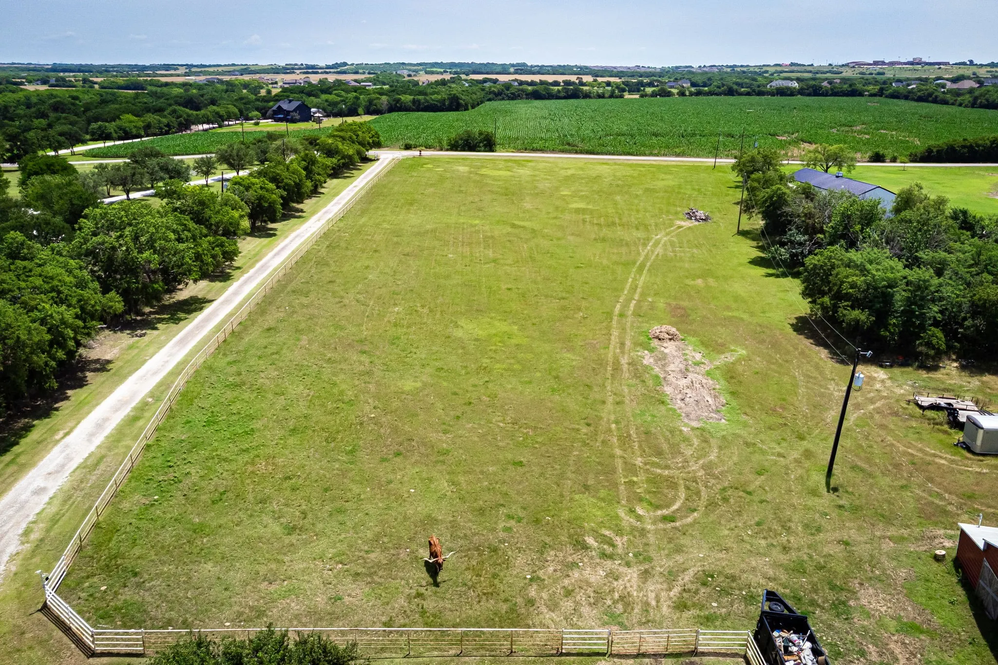 Expansive green acreage featuring a long private driveway, perimeter fencing, mature trees, and a distant field