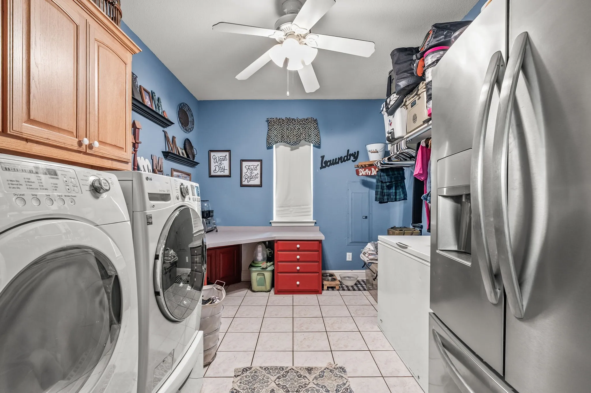 Laundry room featuring tile flooring, built-in wooden cabinetry, a ceiling fan, and a built-in desk area with red drawer storage