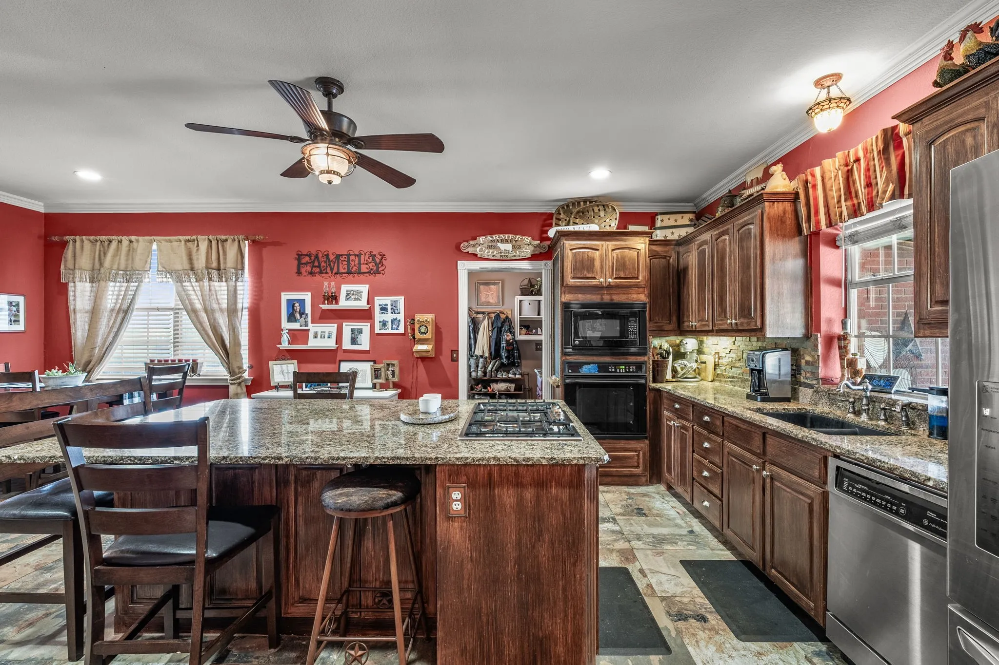 Kitchen featuring a central island with a built-in gas cooktop, granite countertops, custom wood cabinetry, stainless steel appliances, and wood-finish flooring