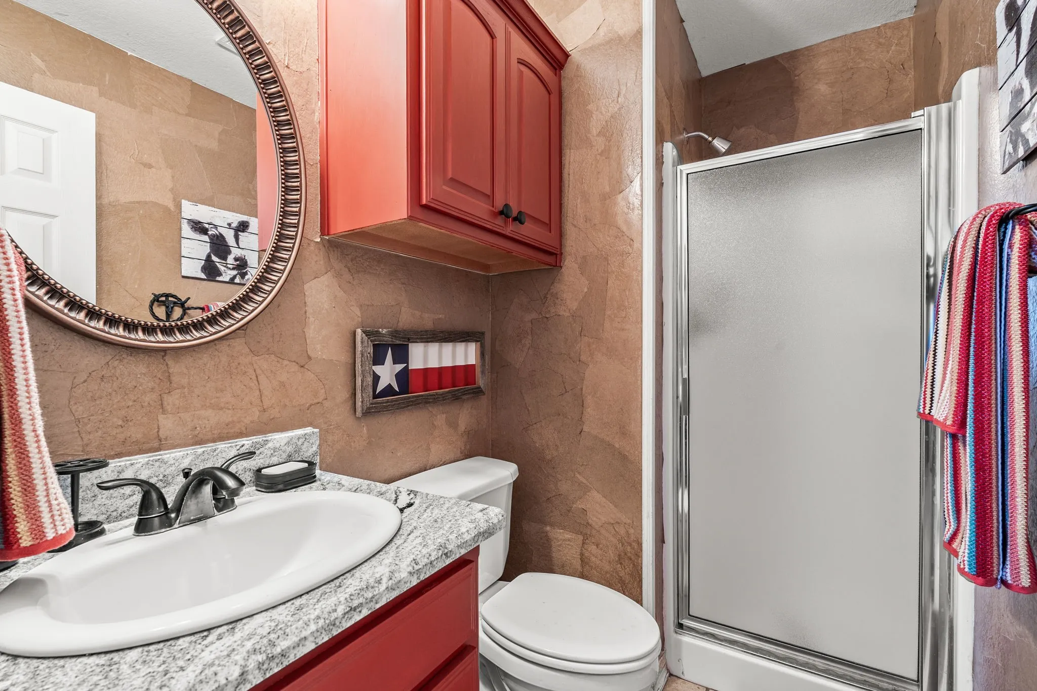 Bathroom featuring a glass-enclosed shower, white toilet, and a vanity with a white basin and speckled countertop