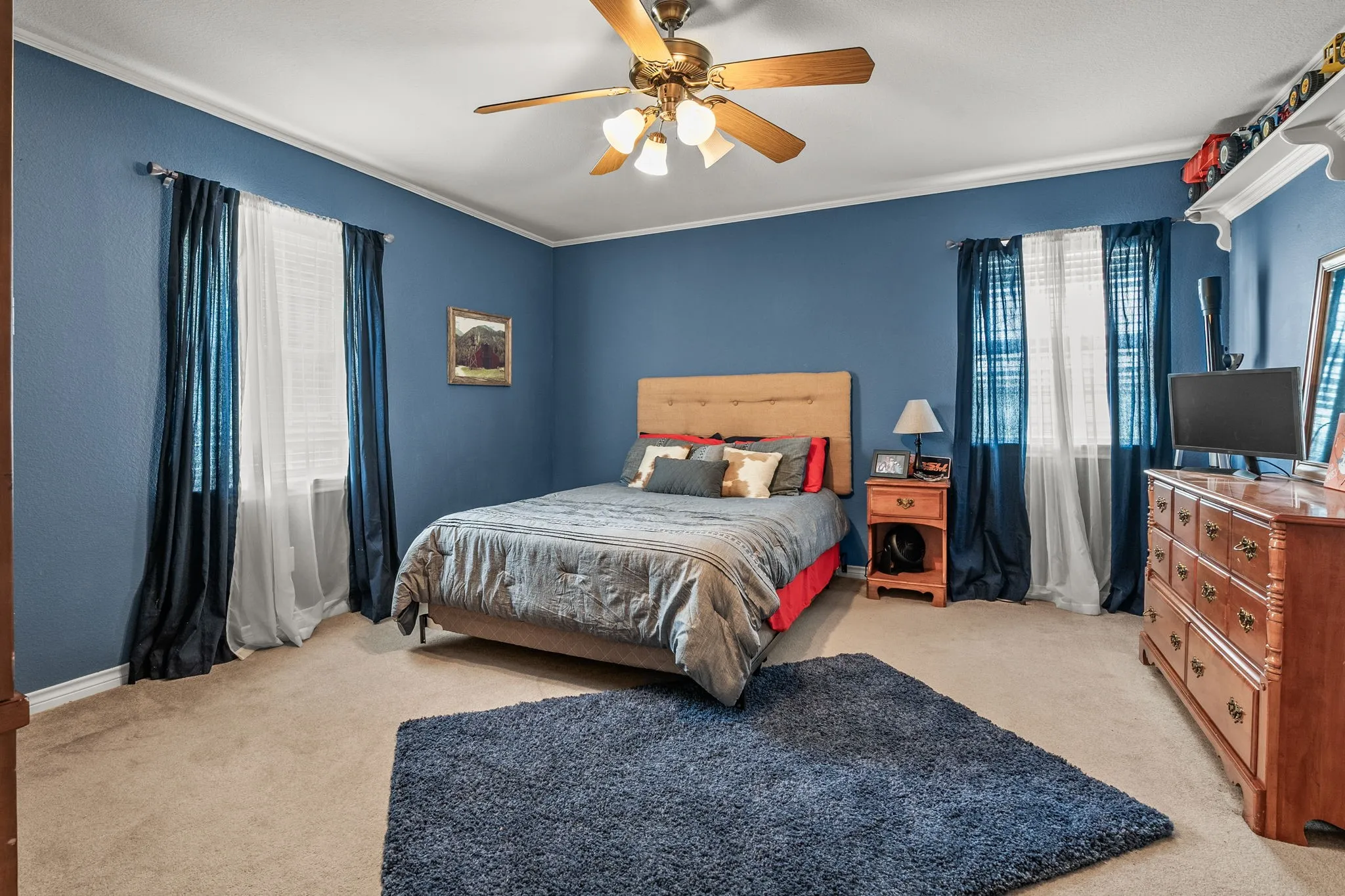 Carpeted room featuring a ceiling fan with integrated lighting, crown molding, and two windows with blinds
