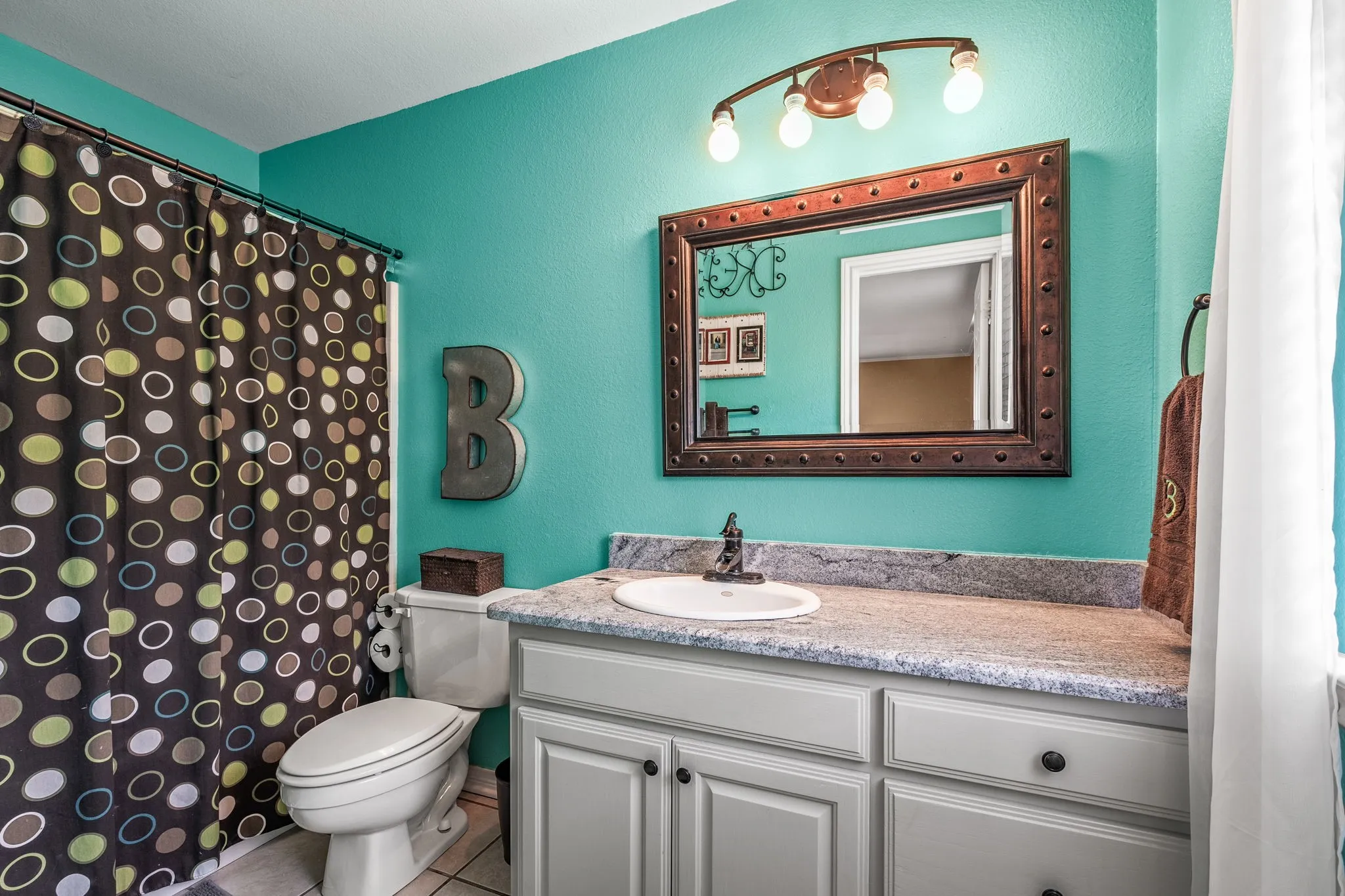 Bathroom featuring a vanity with a white countertop and undermount sink, a framed mirror, a wall-mounted light fixture, and a toilet
