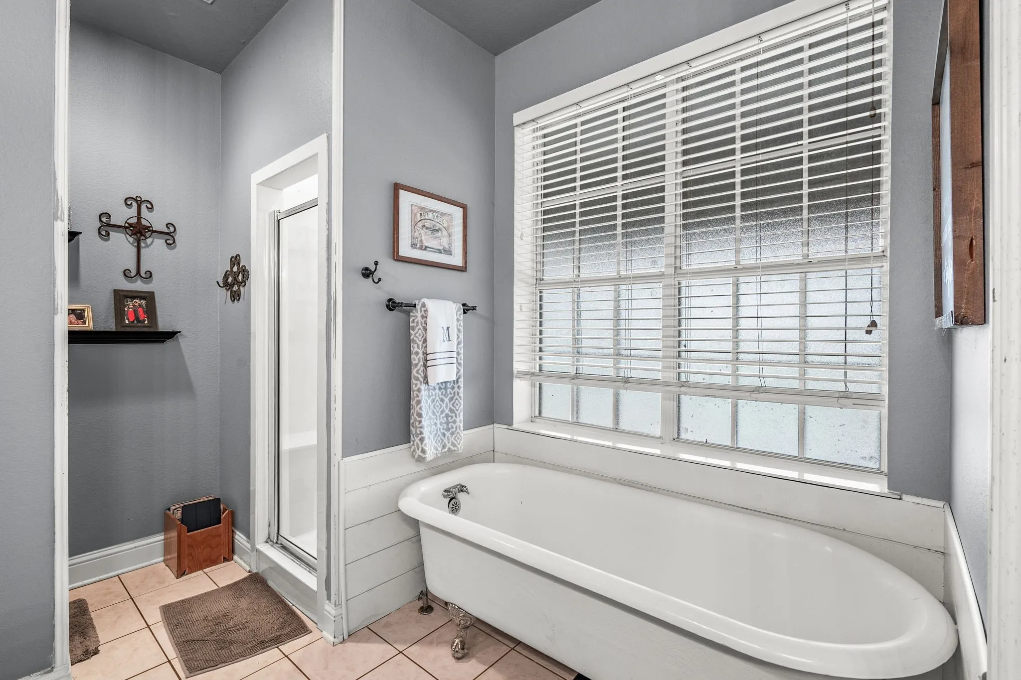 Bathroom featuring a clawfoot tub, a separate shower enclosure with a glass door, a large window with blinds, and light-toned tile flooring